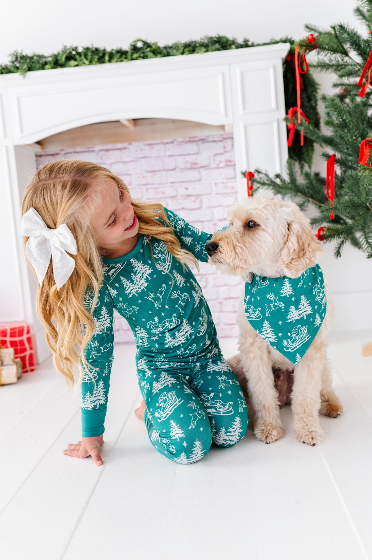 A little girl and her dog sitting in front of a fireplace and a Christmas tree. They're watching matching bamboo styles featuring vintage Santa and his reindeer 