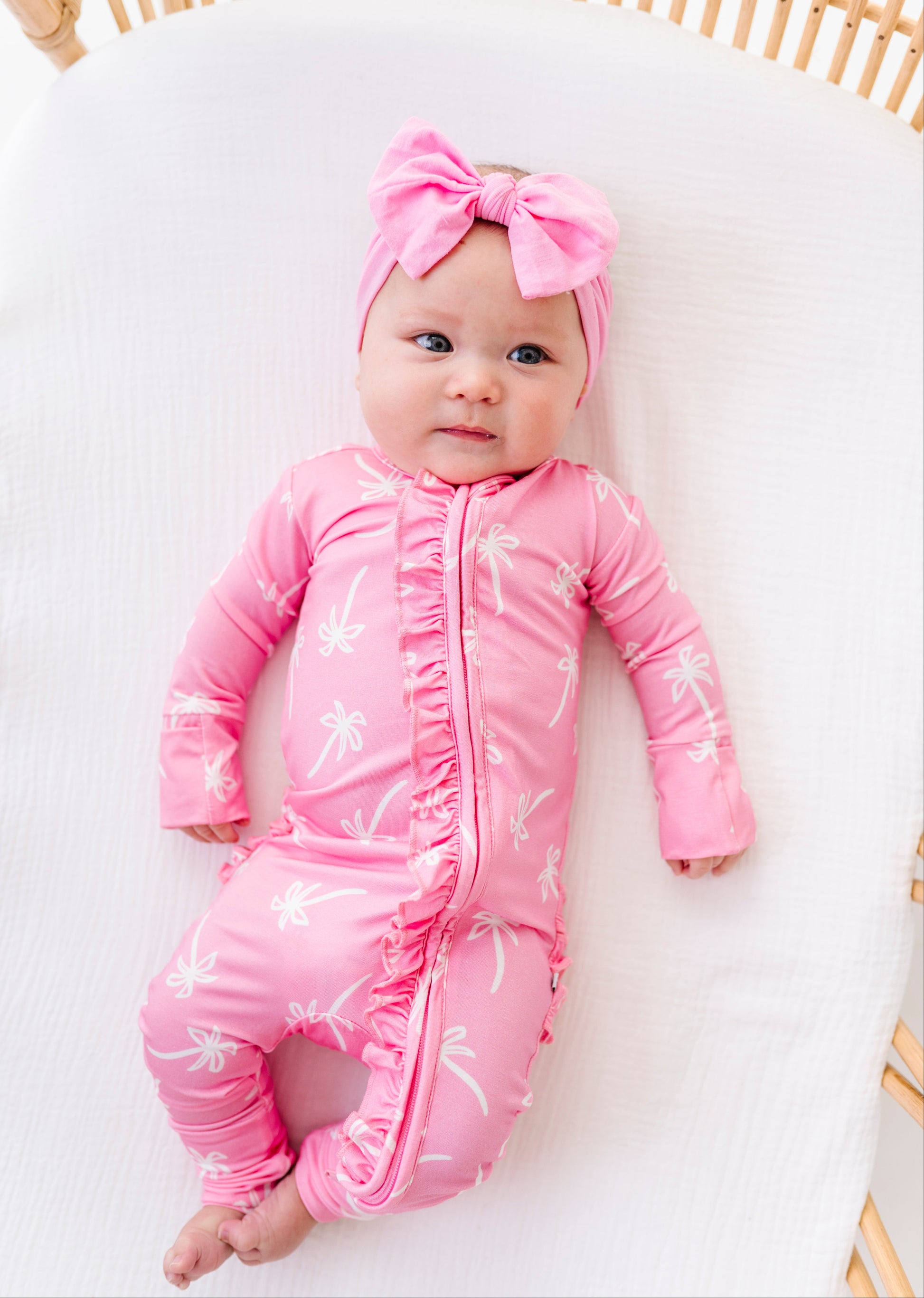 Baby in a pink outfit with a bow lying on a white surface