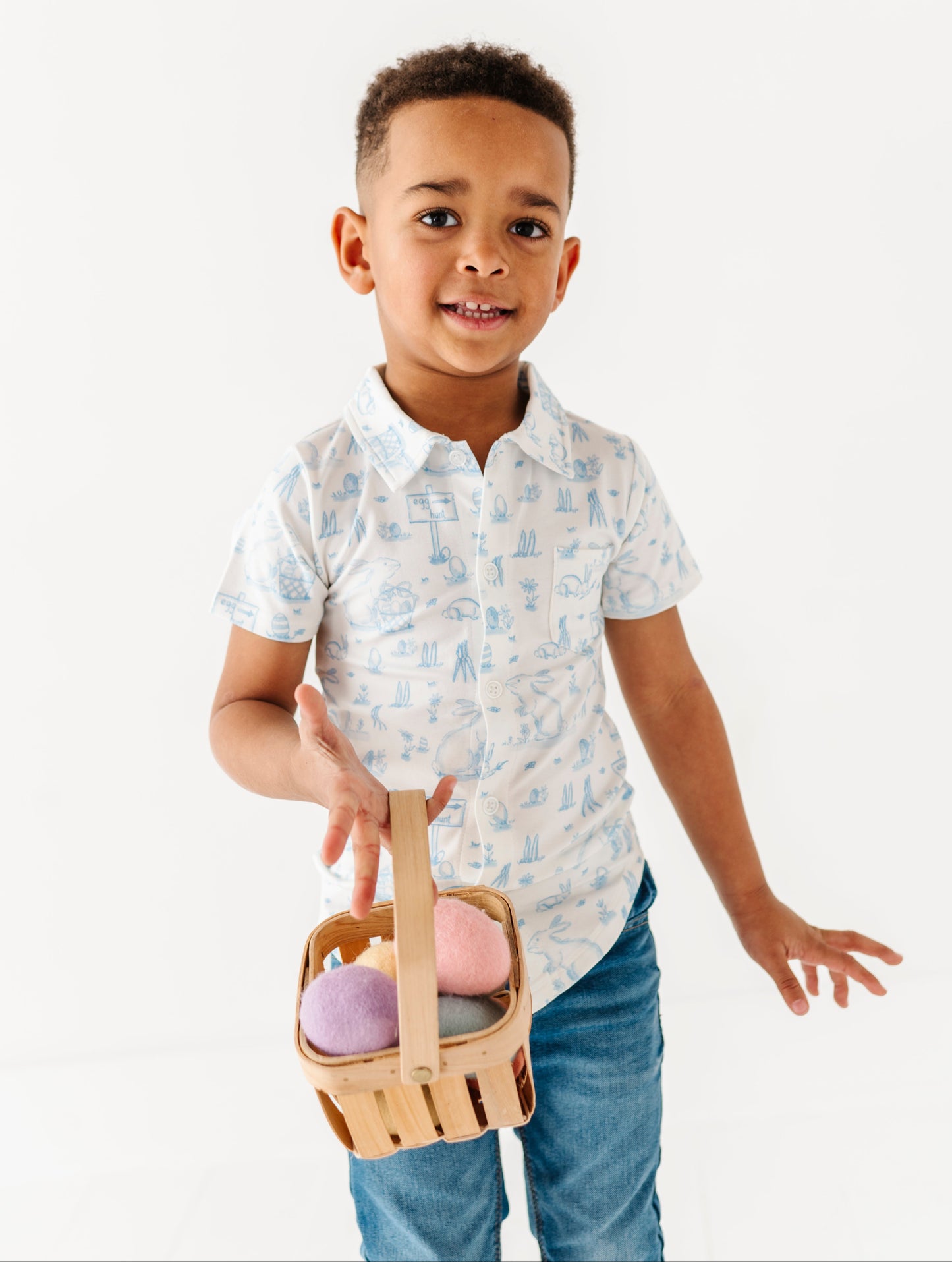 Child holding a small wooden basket with pastel-colored items on a white background