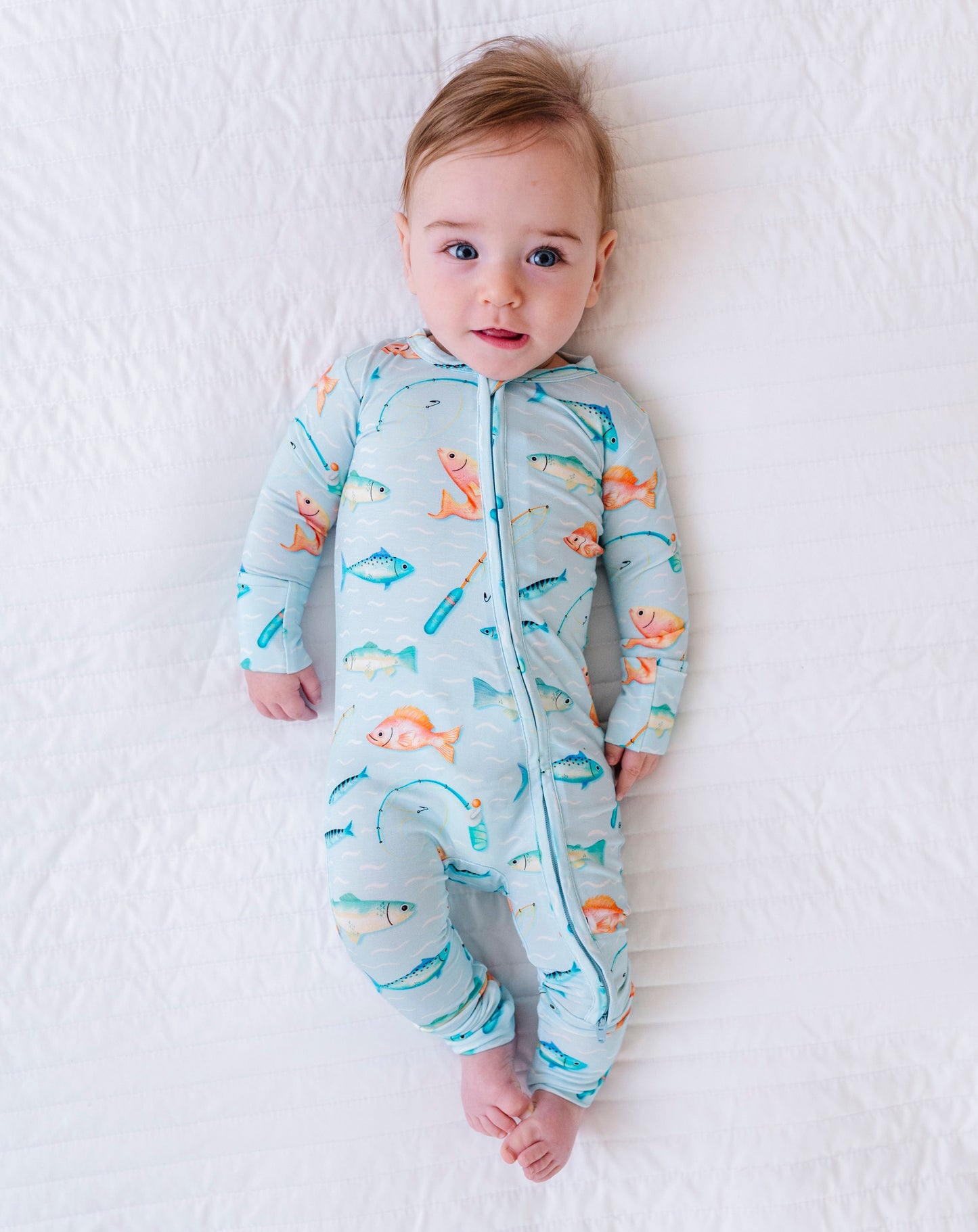 Baby wearing a colorful onesie with fish patterns on a white blanket