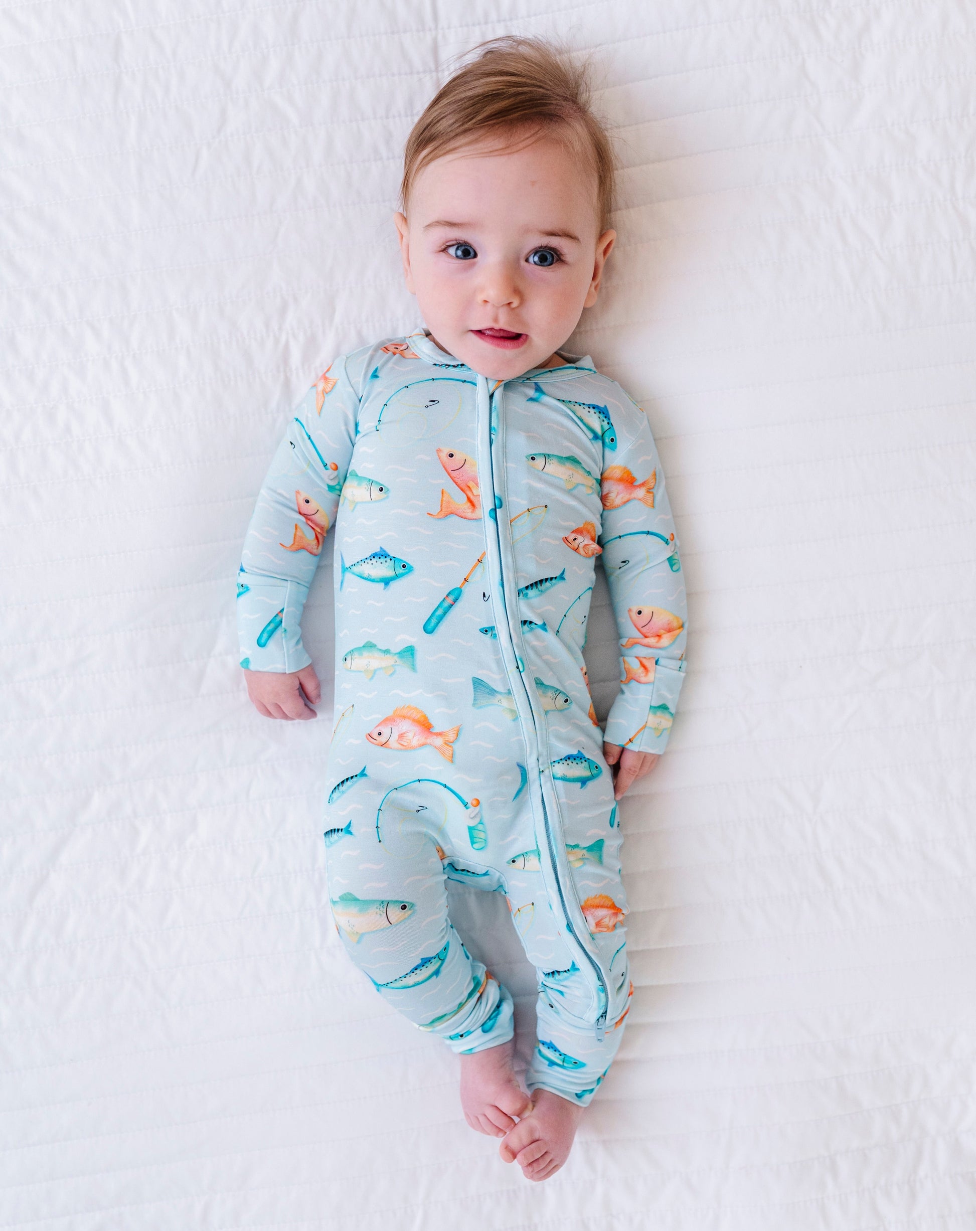 Baby wearing a colorful onesie with fish patterns on a white blanket