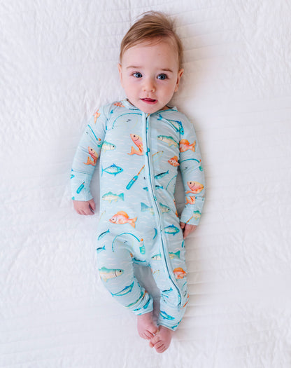 Baby wearing a colorful onesie with fish patterns on a white blanket