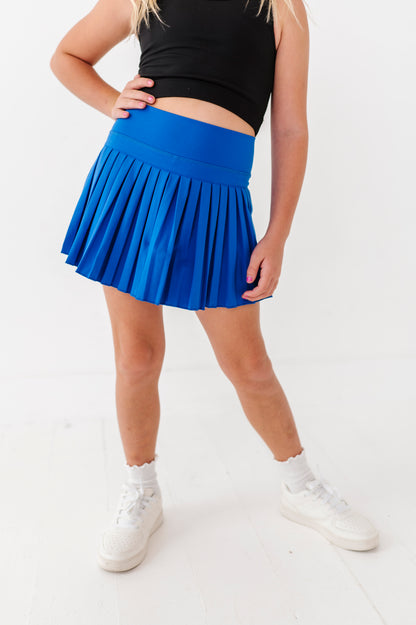 Person wearing a blue pleated active skort and black top on a white background