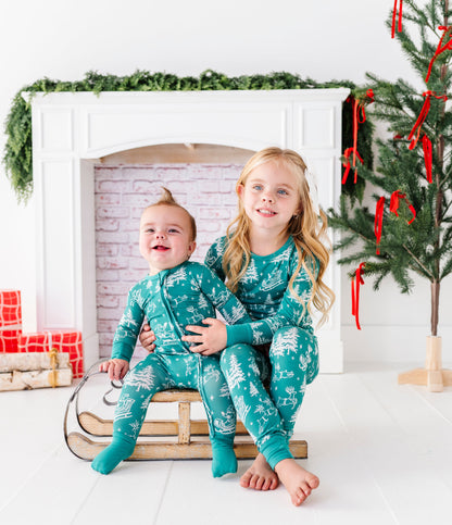 A brother and sister sitting on a wooden sleigh. They're wearing matching bamboo pajamas featuring vintage Santa and his reindeer 