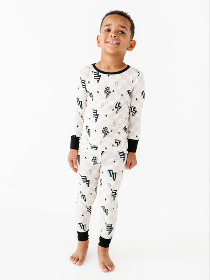 A young boy wearing a long-sleeve white pajama set with a black graphic pattern, standing against a plain white studio background.