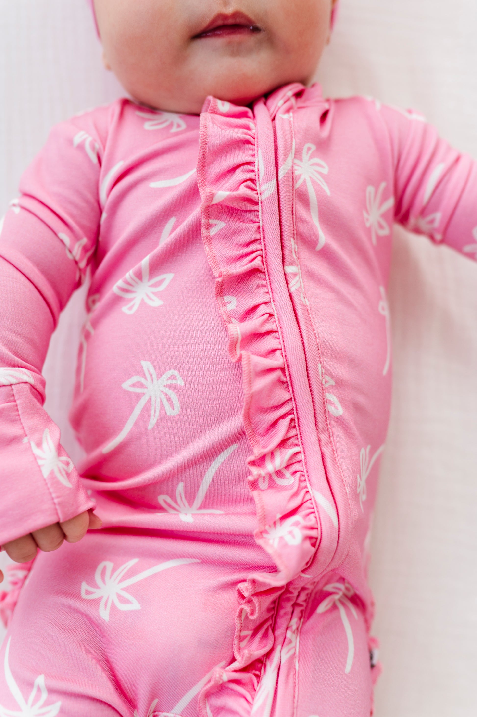 Baby wearing a pink outfit with white palm tree  patterns on a light background