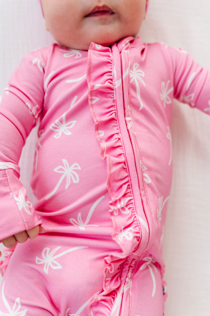 Baby wearing a pink outfit with white palm tree  patterns on a light background
