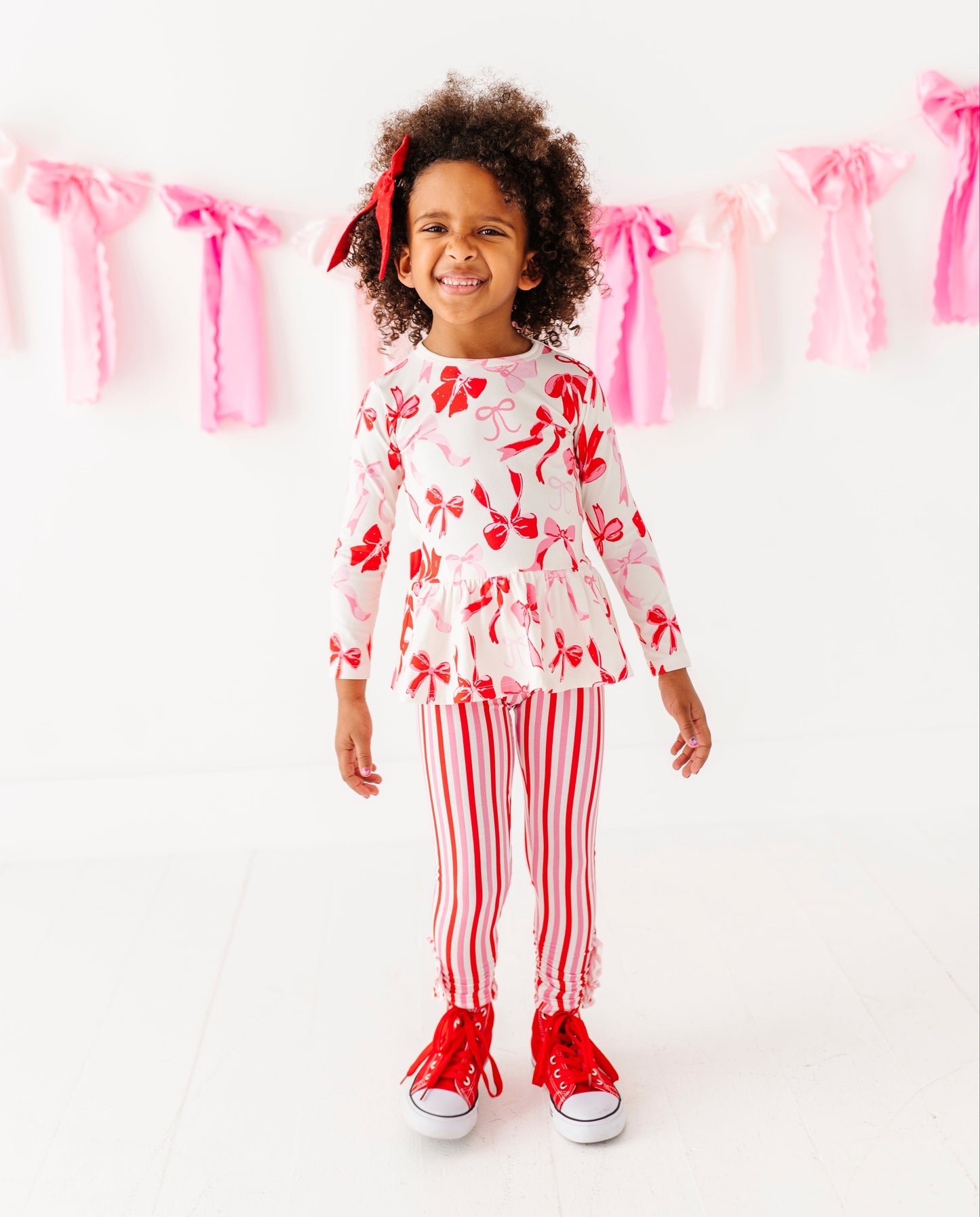 Girl standing in Blushing Bows peplum top and pink striped bottoms