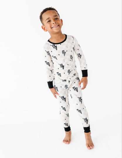 A young boy smiling and wearing a long-sleeve white pajama set with a black geometric pattern, photographed against a seamless white studio background.