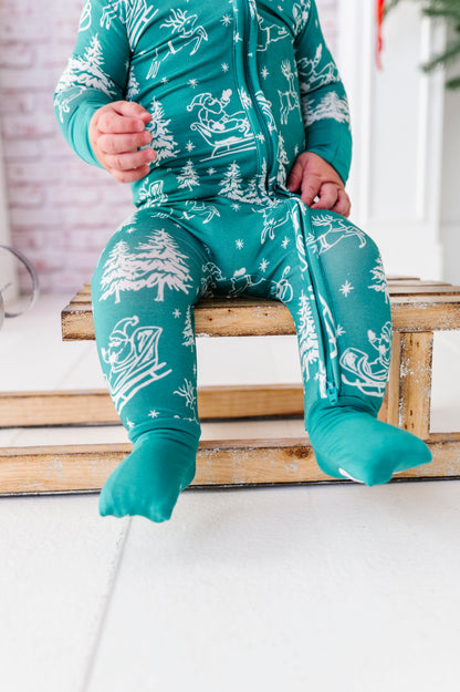 A close-up detail shot of a little boy sitting on a wooden sleigh and wearing a bamboo zip romper with Santa and his sleigh 