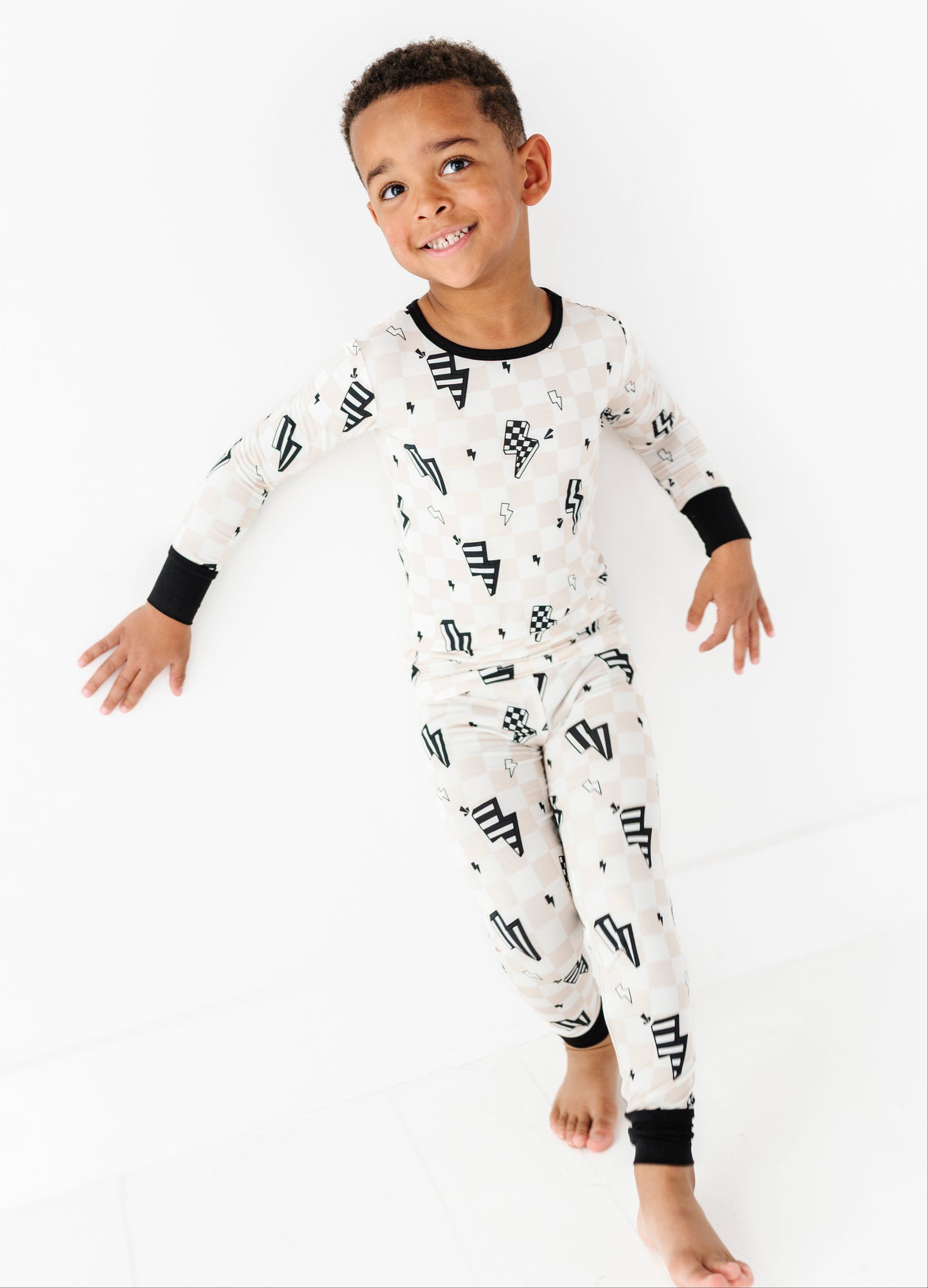 A young boy wearing a long-sleeve white pajama set with a black geometric pattern, standing against a clean white background.