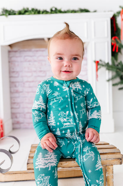 A baby boy wearing a bamboo convertible romper featuring vintage scenery with Santa and his reindeer 