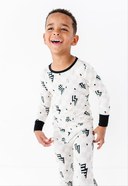 A young boy smiling and laughing while wearing a white long-sleeve pajama set with black graphic patterns and black trim on the collar and cuffs, set against a plain white studio background.