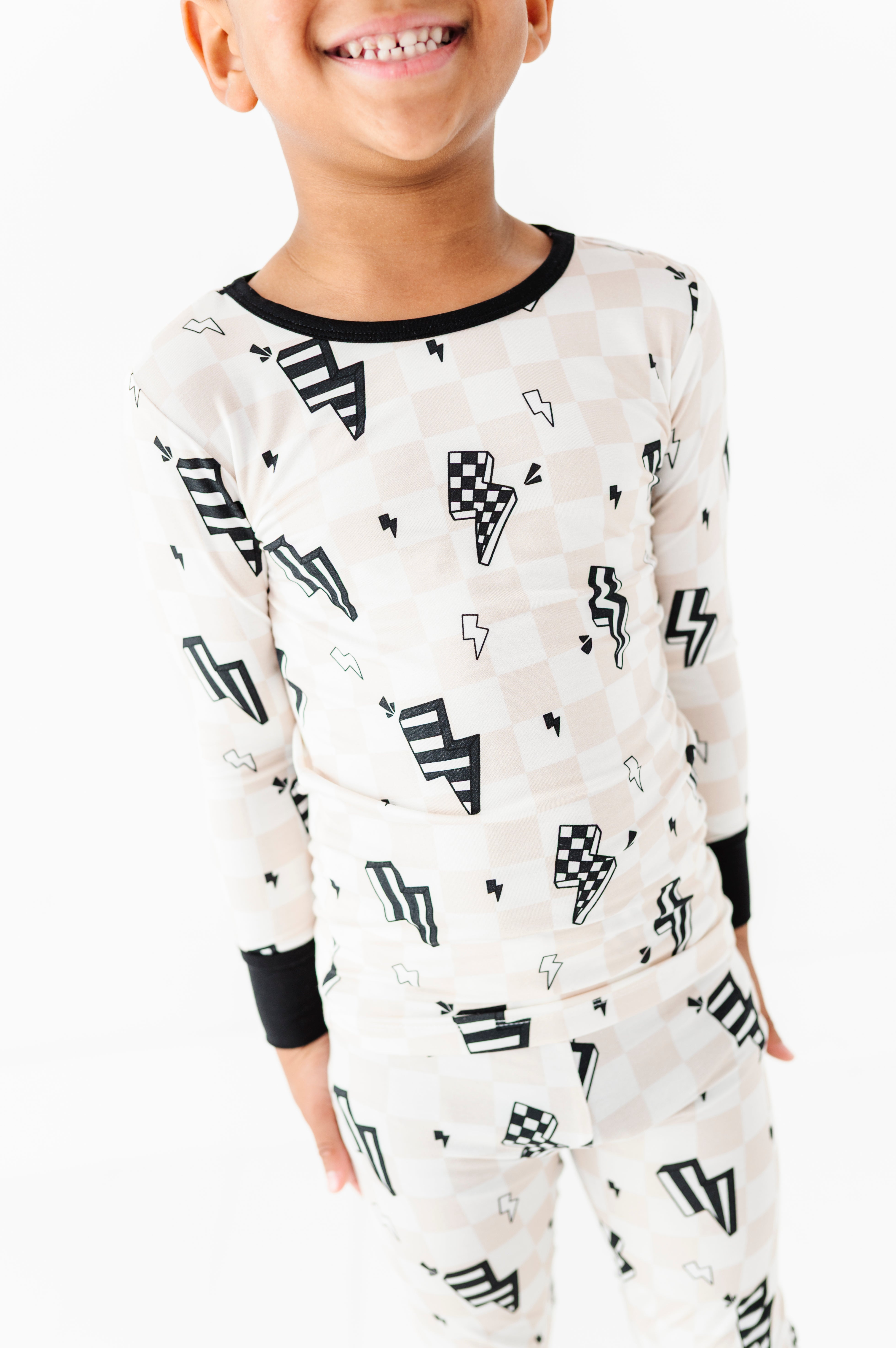 A child wearing a long-sleeve pajama set with a black and white lightning bolt and checkerboard pattern, shown against a plain white background.
