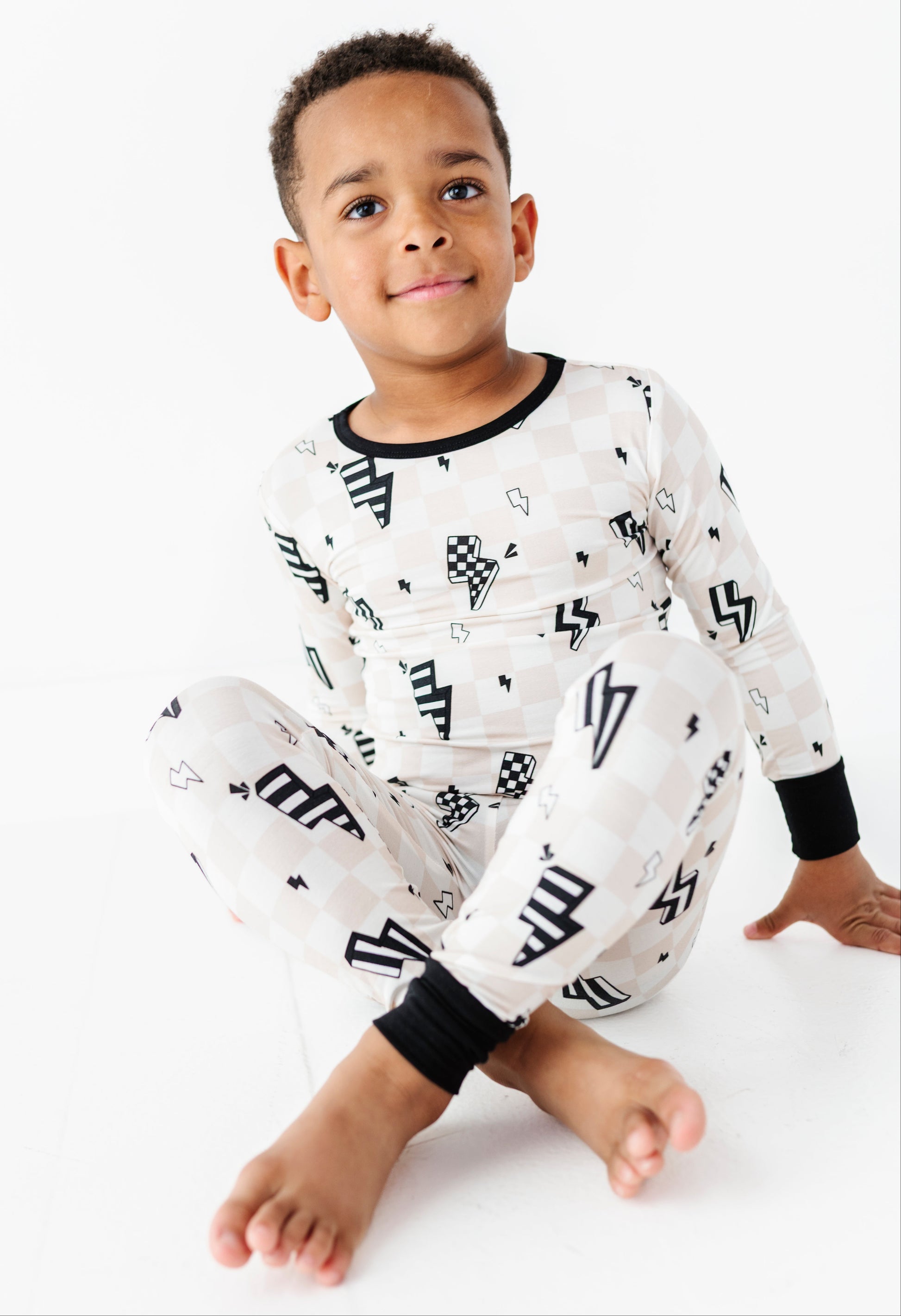 A young boy wearing a white long-sleeve pajama set with black graphic patterns, sitting cross-legged against a plain white background.