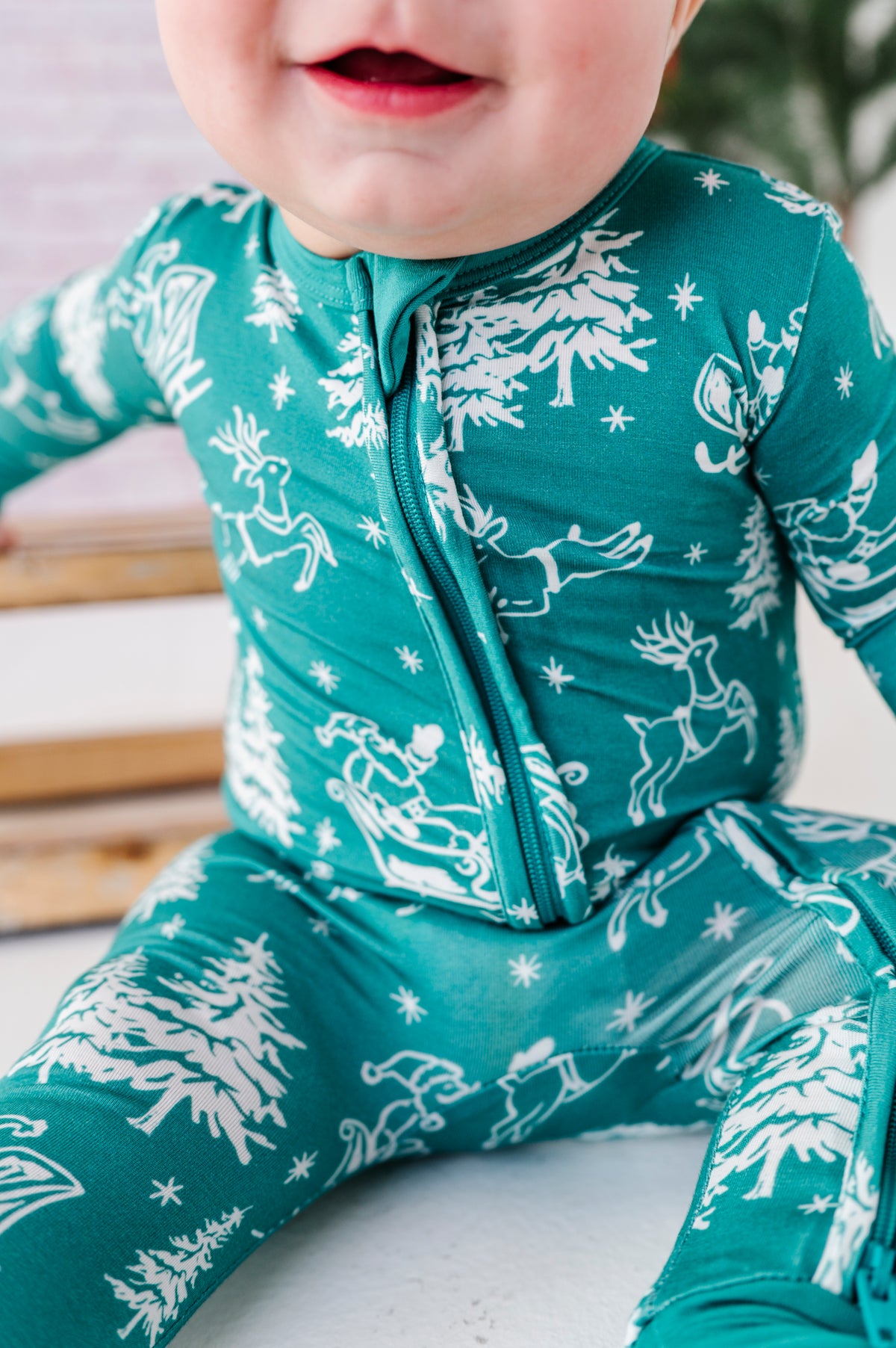 A close-up detail shot of a bamboo zip romper on a baby. The convertible romper features vintage scenes of Santa and his reindeer 