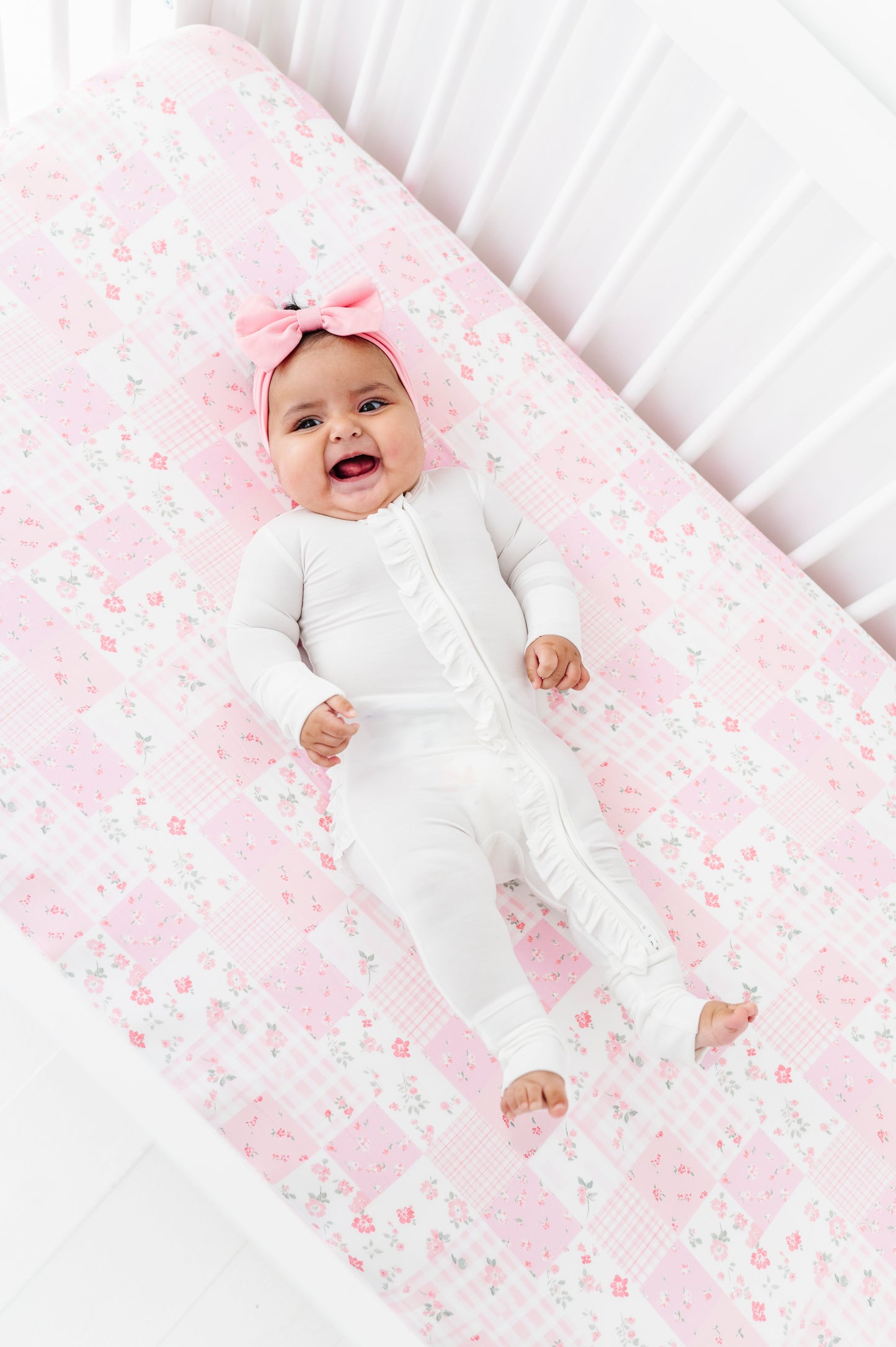 Baby lying on a pink bamboo crib sheet with a white crib in the background