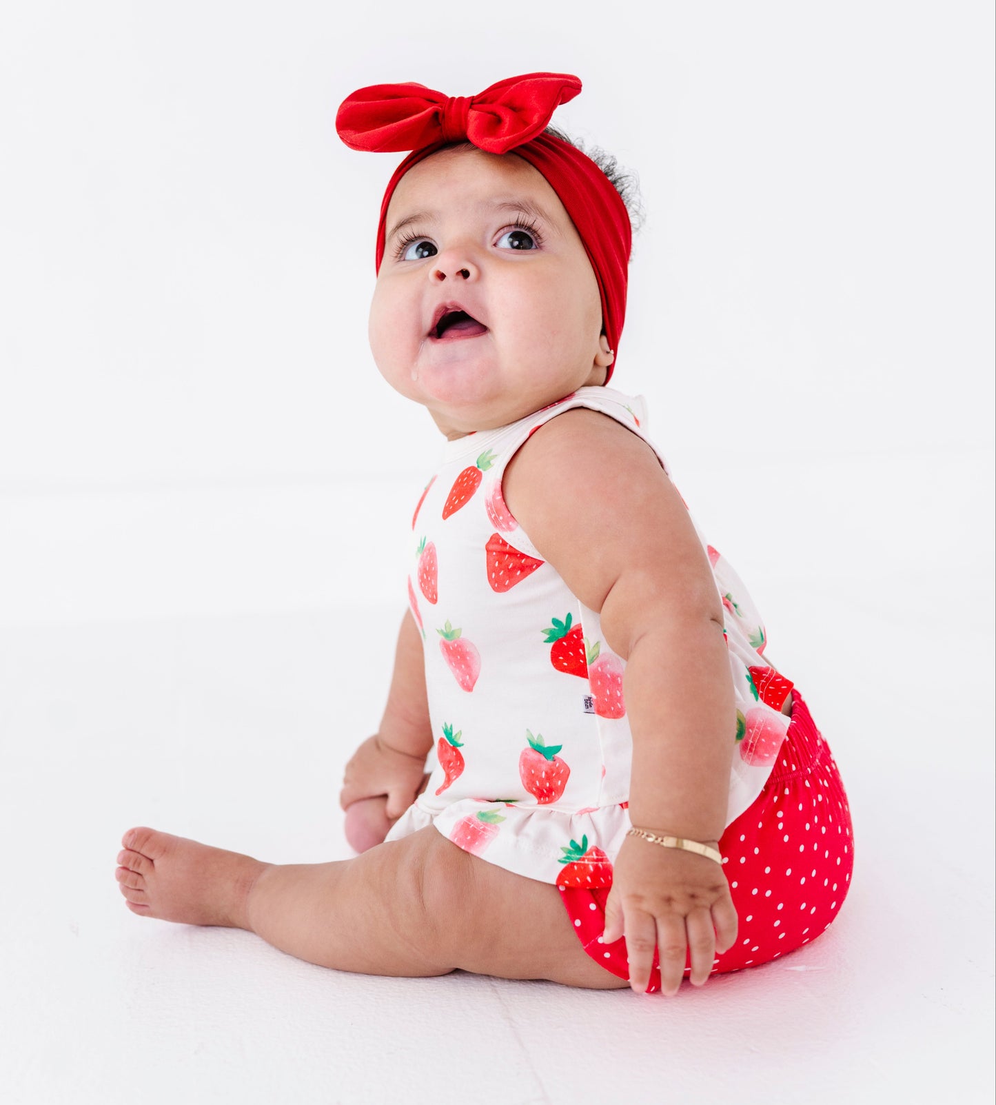 Baby wearing a strawberry-patterned outfit with a red bow on a white background