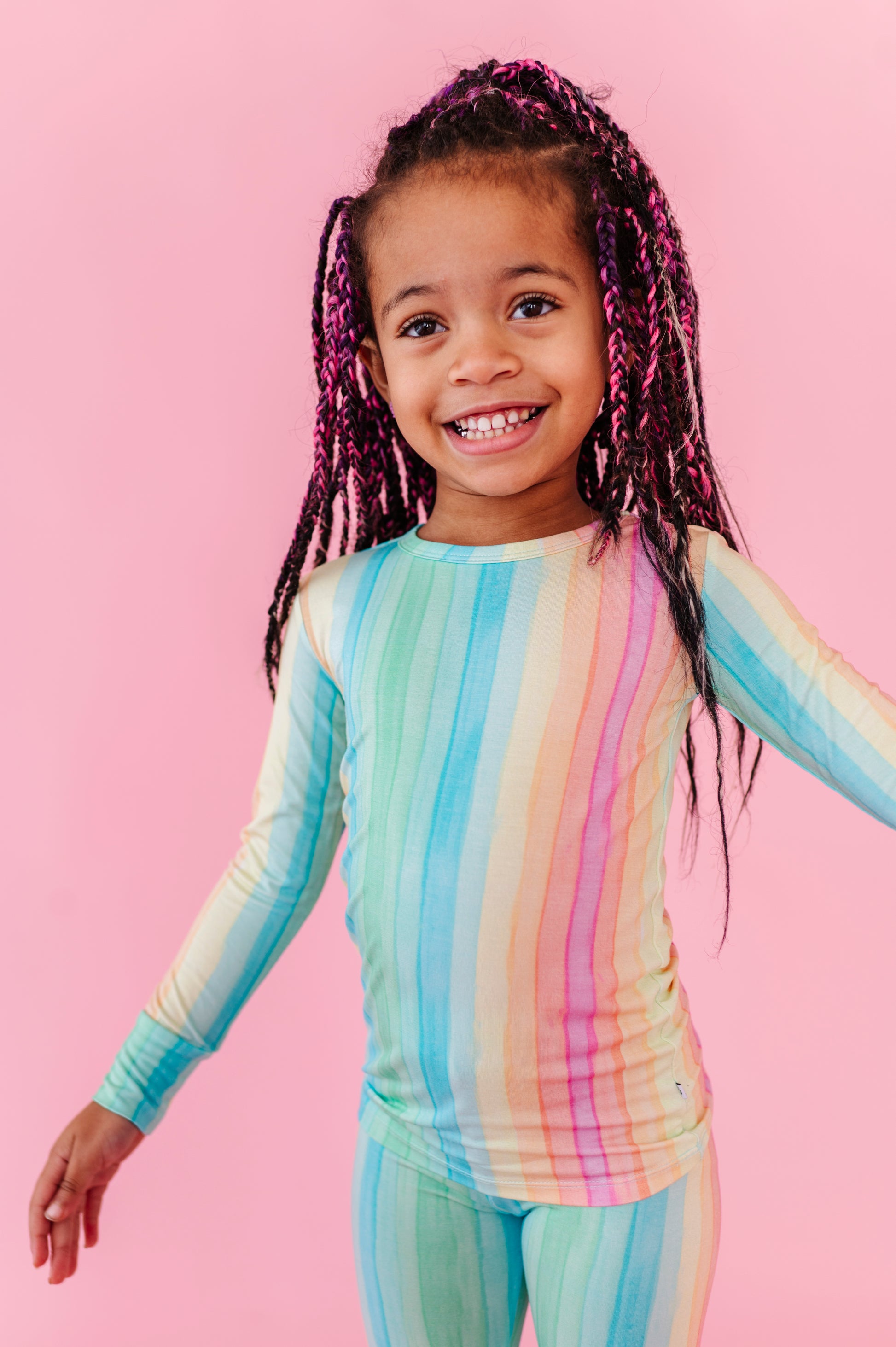 Child wearing a rainbow striped bamboo pajama set on a pink background