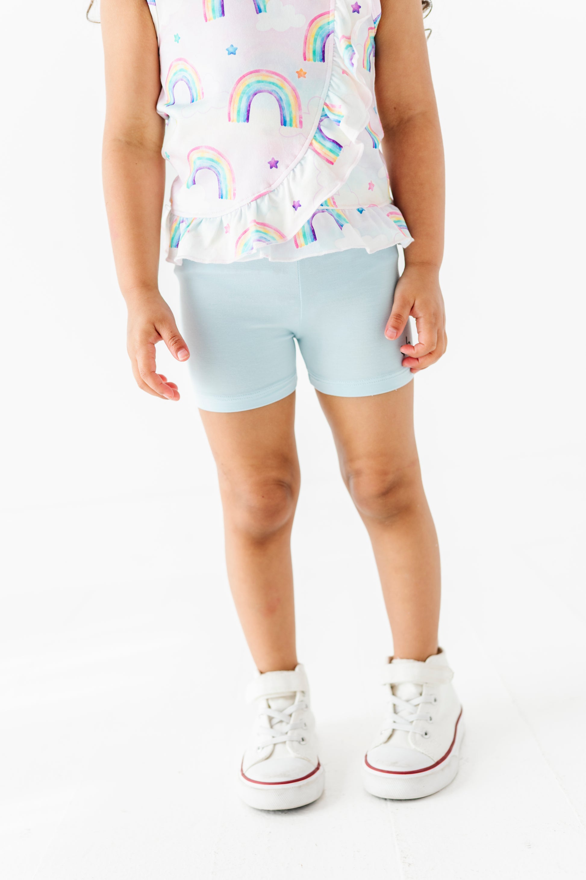 Child wearing a bamboo cotton peplum top with watercolor rainbow patterns and light blue bamboo biker shorts on a white background