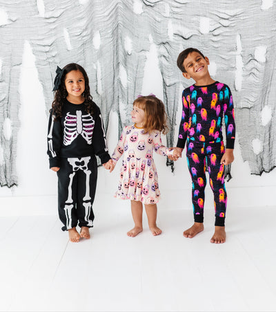 Three children wearing colorful pajamas standing in front of a decorative white wall with black patterns.