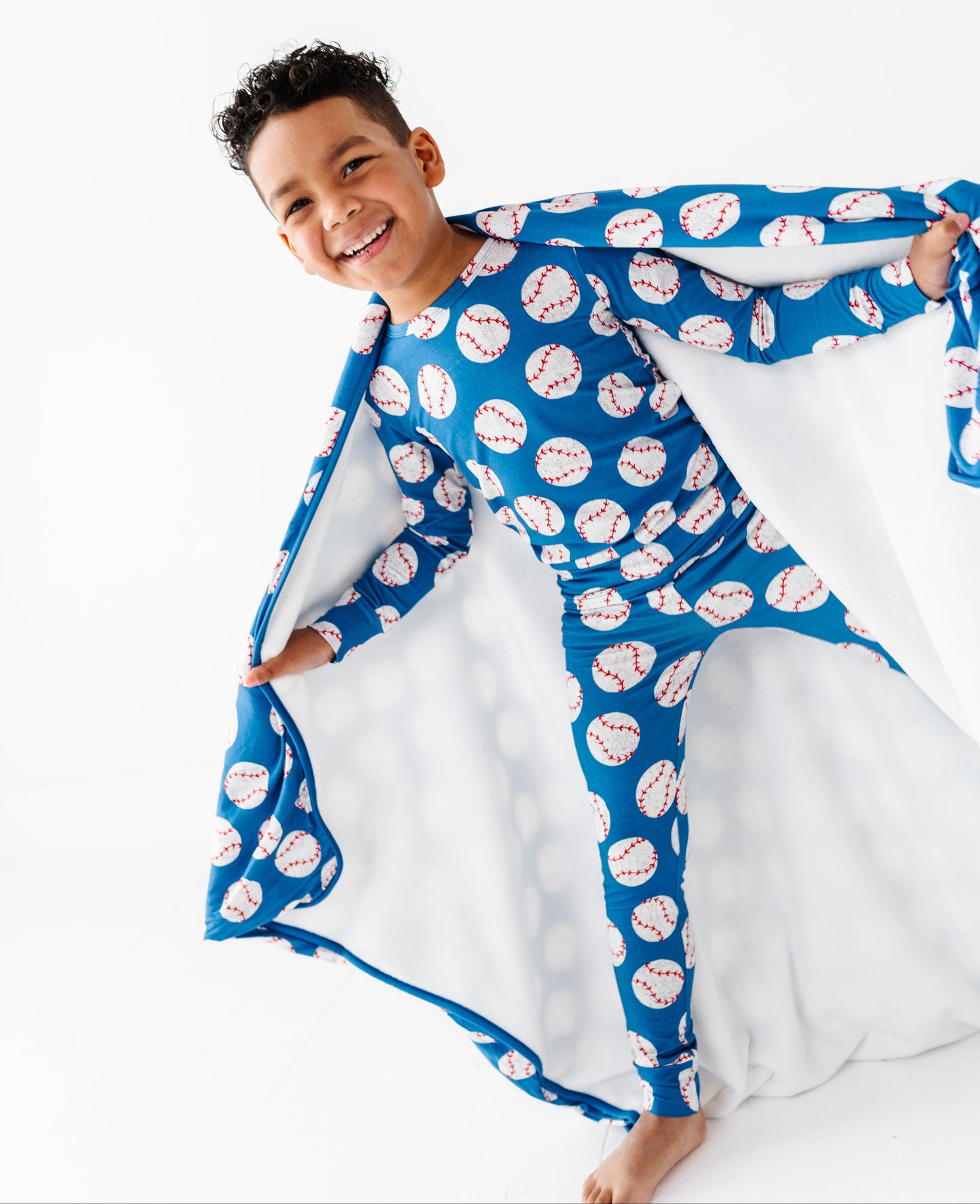 Child holding a blue blanket with white baseballs on a white background