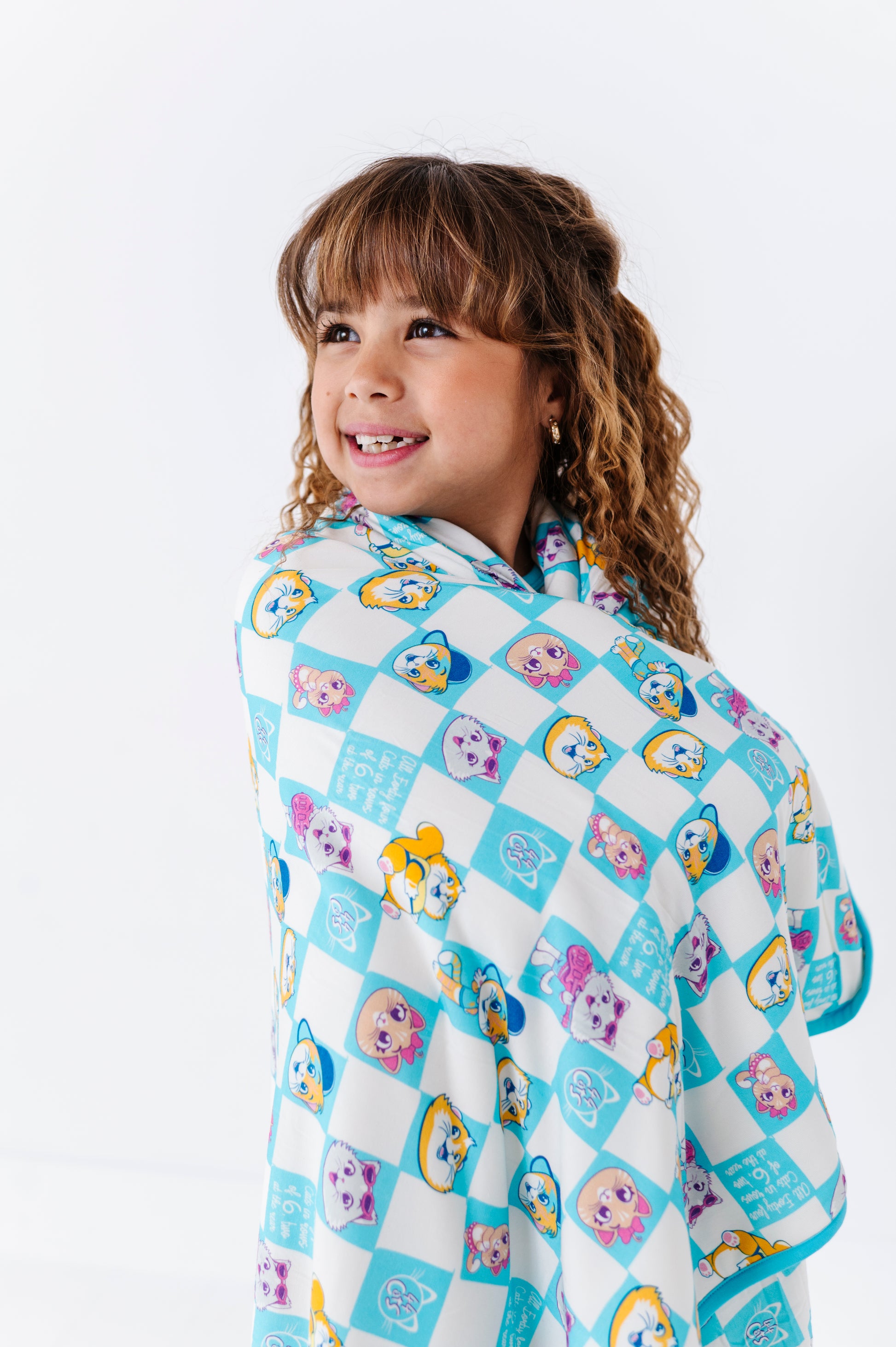 Child wrapped in a 44 Cats bamboo blanket with cartoon characters on a white background