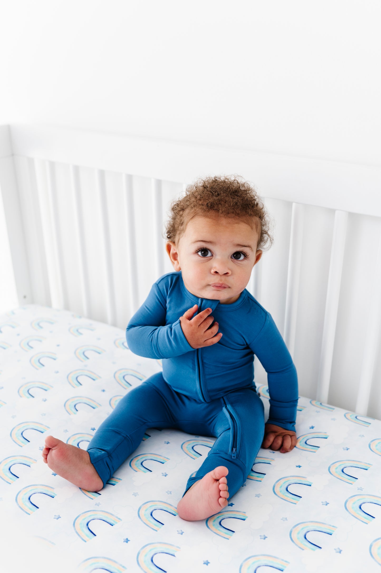 Child wearing a blue bamboo convertible romper on a crib with a white background