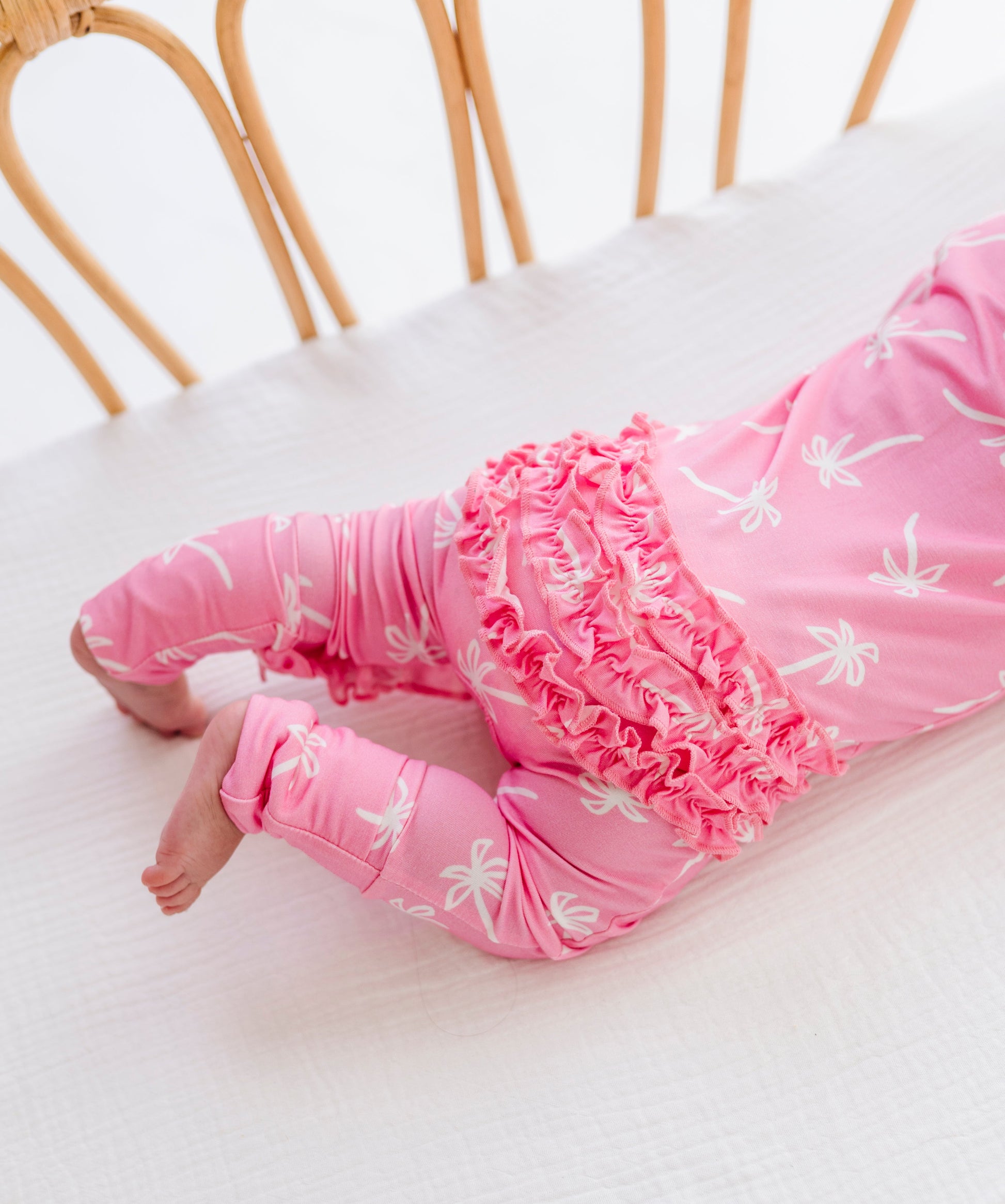 Baby in pink outfit with floral patterns lying on a white surface.