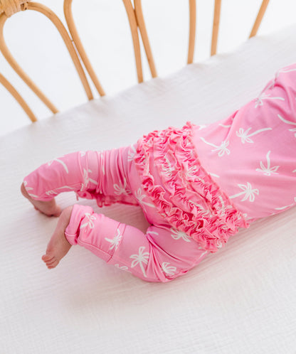 Baby in pink outfit with floral patterns lying on a white surface.