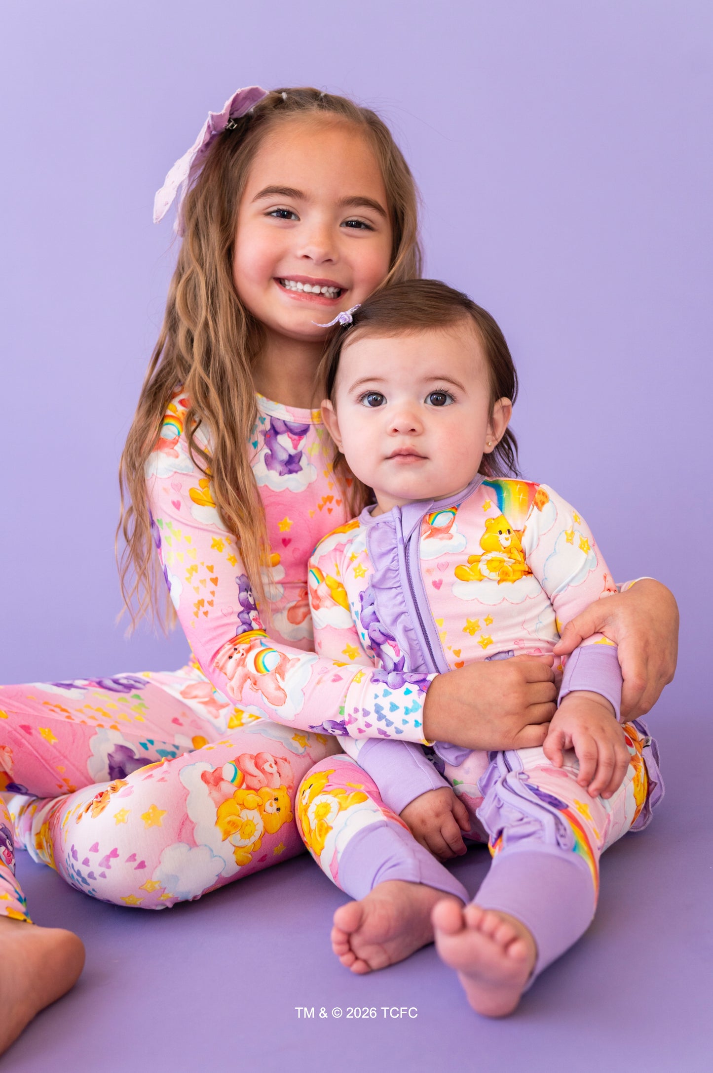 Two children in colorful pajamas sitting on a purple background