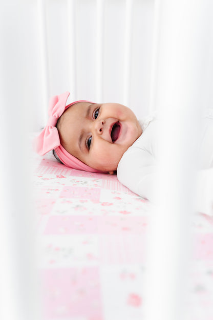 Baby wearing a pink headband with a bow, lying on a bamboo crib sheet with pink polka dots.