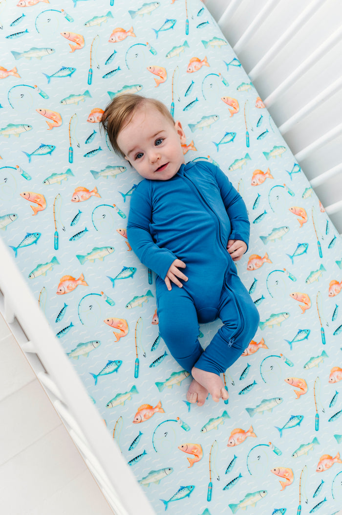 Baby lying on a crib with a colorful fish patterned bamboo sheet