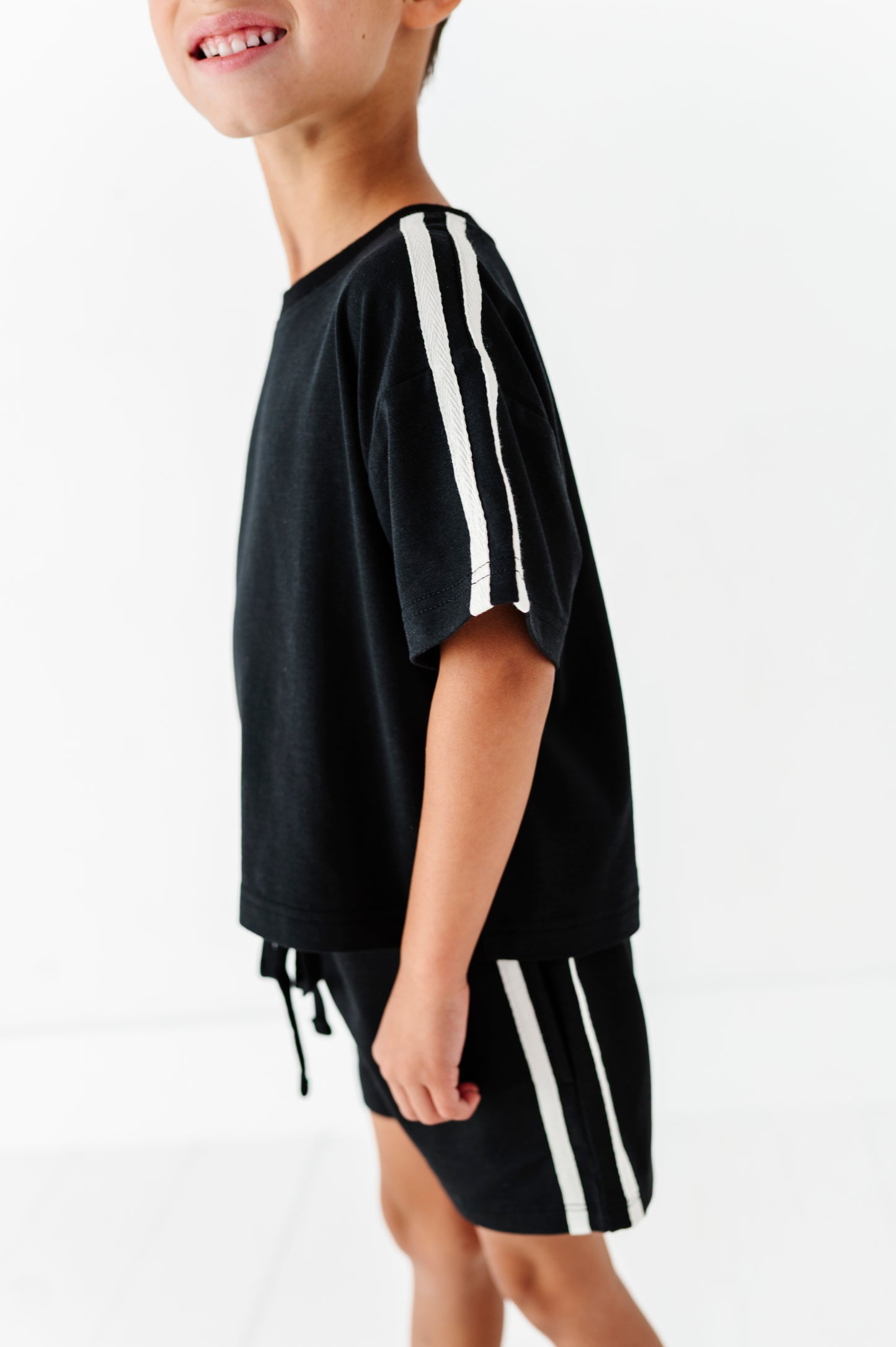 A child wearing a black short-sleeve t-shirt and matching shorts, both featuring white vertical stripes down the sleeves and sides, photographed against a clean white background.