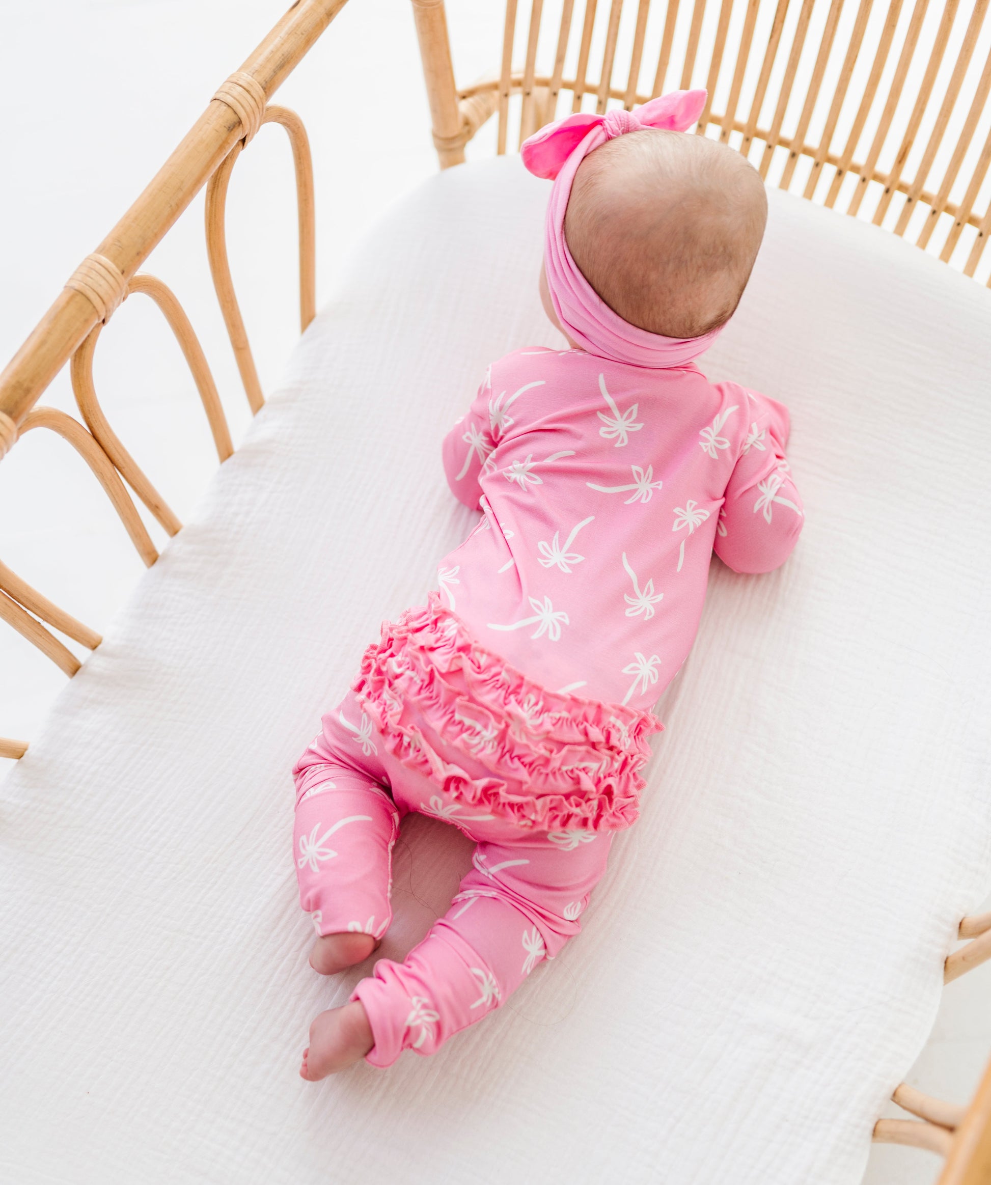 Baby in a pink outfit lying in a crib with white bedding