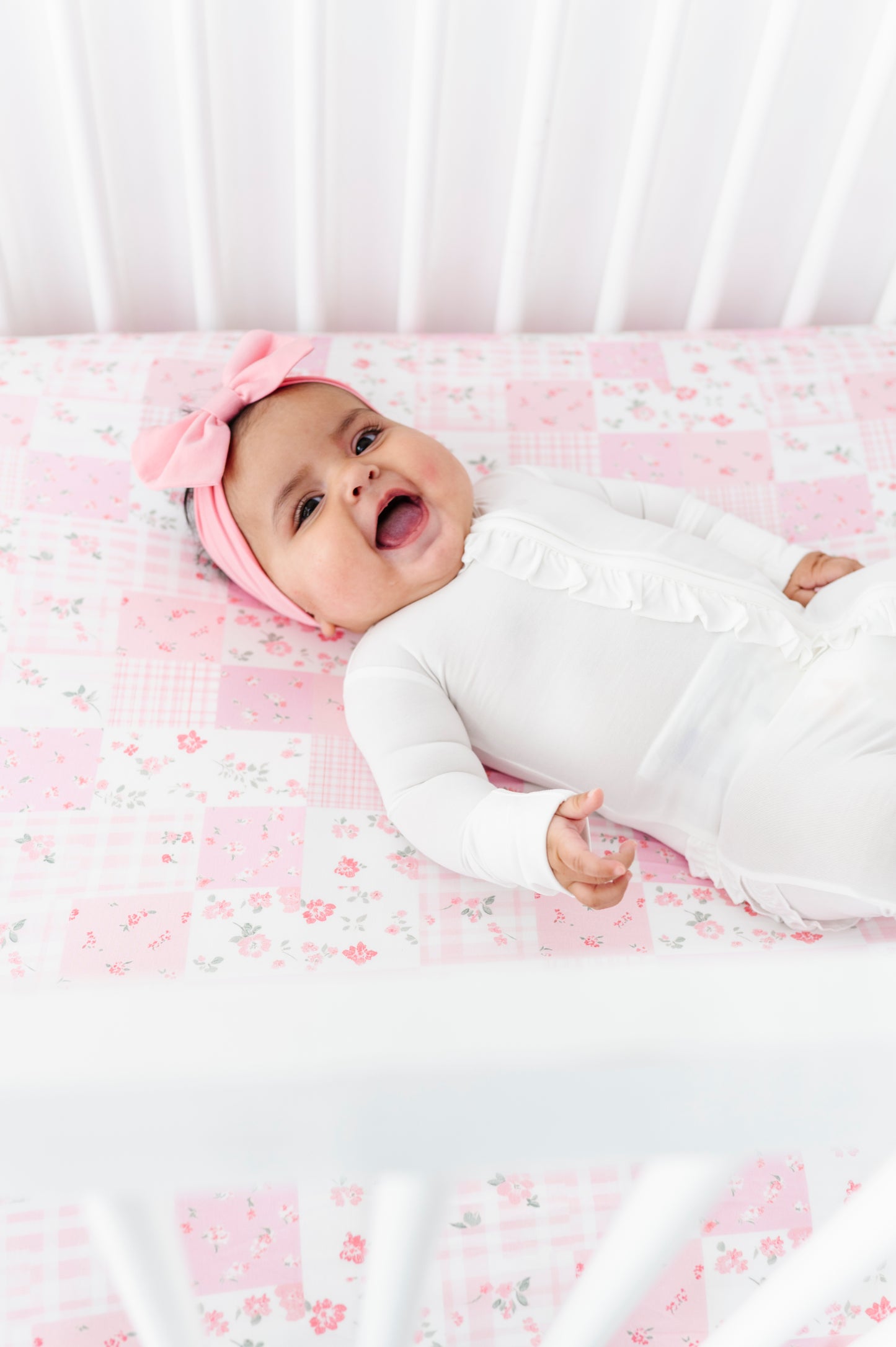 Infant wearing a white bamboo zip romper and laying on a pink patchwork bamboo crib sheet 
