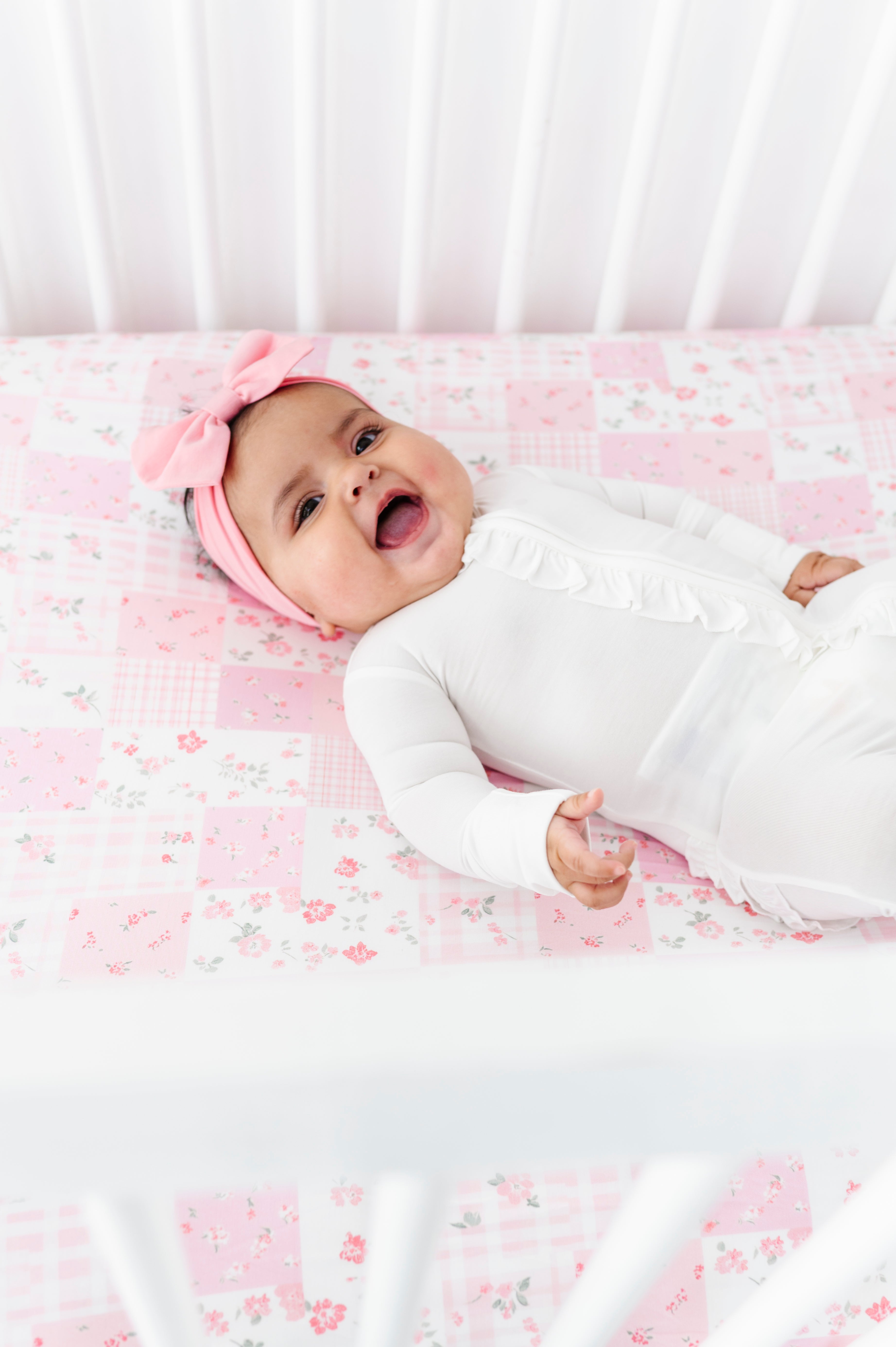 Infant wearing a white bamboo zip romper and laying on a pink patchwork bamboo crib sheet 