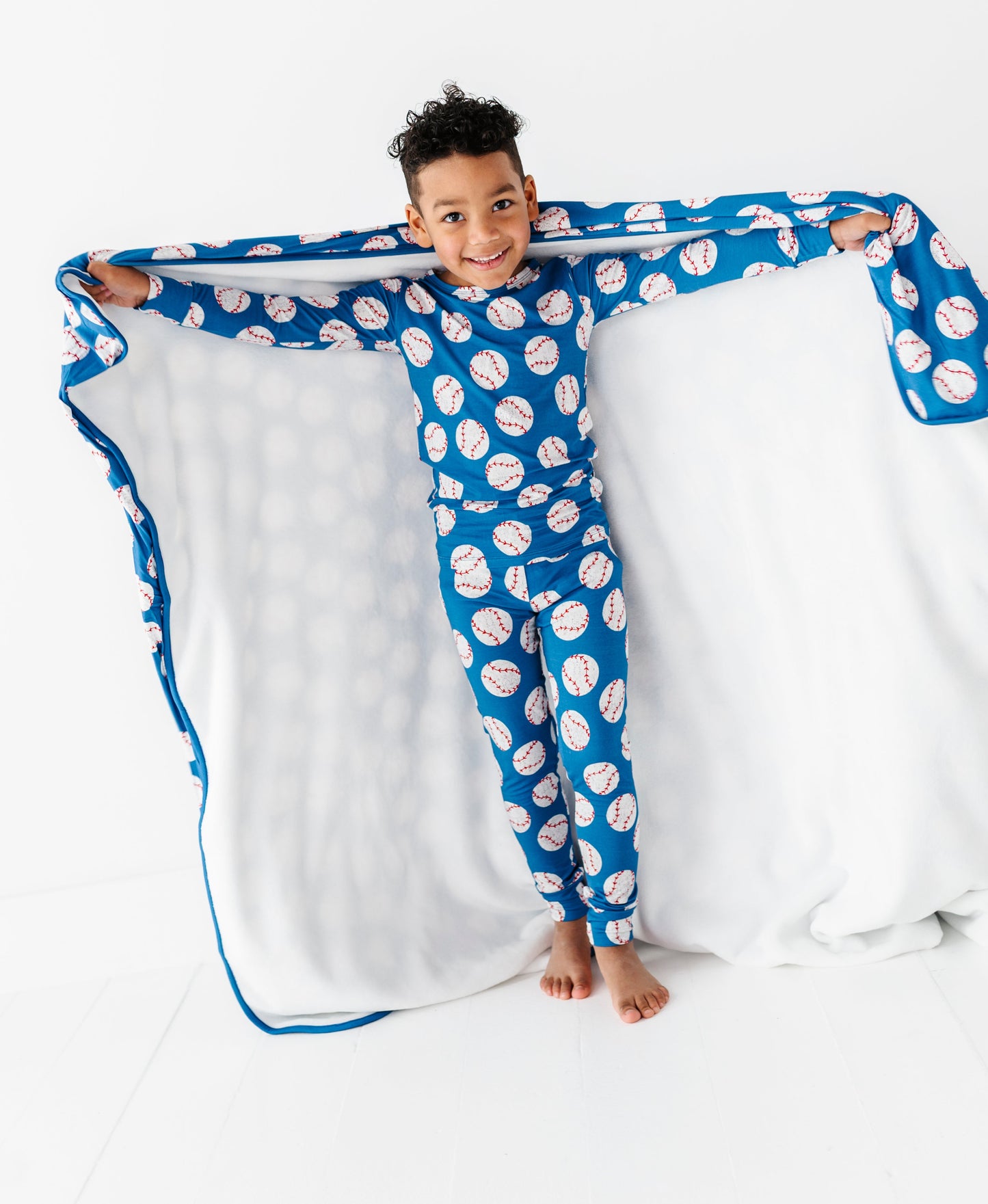 Child wearing a blue and white baseball patterned bamboo pajama set with a matching blanket.