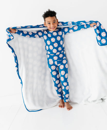 Child wearing a blue and white baseball patterned bamboo pajama set with a matching blanket.