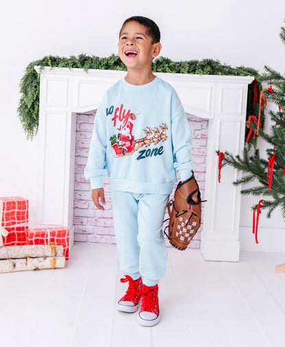 A little boy laughing and wearing an all-light blue outfit. His clothes show Santa catching a baseball in his sleigh 
