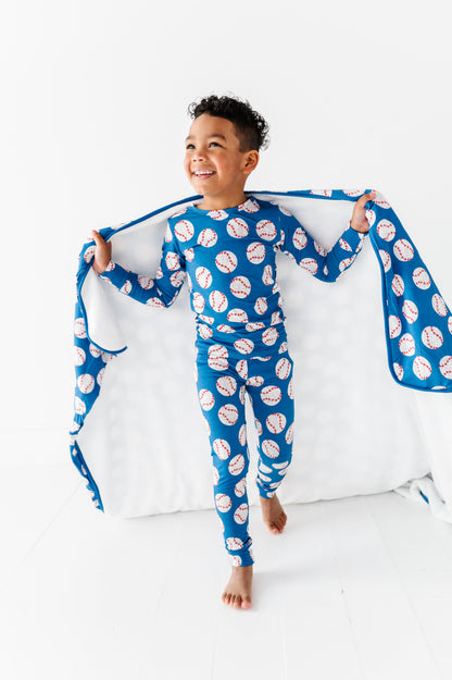 Young boy wearing a bamboo pajama set featuring baseballs and carrying a matching bamboo blanket
