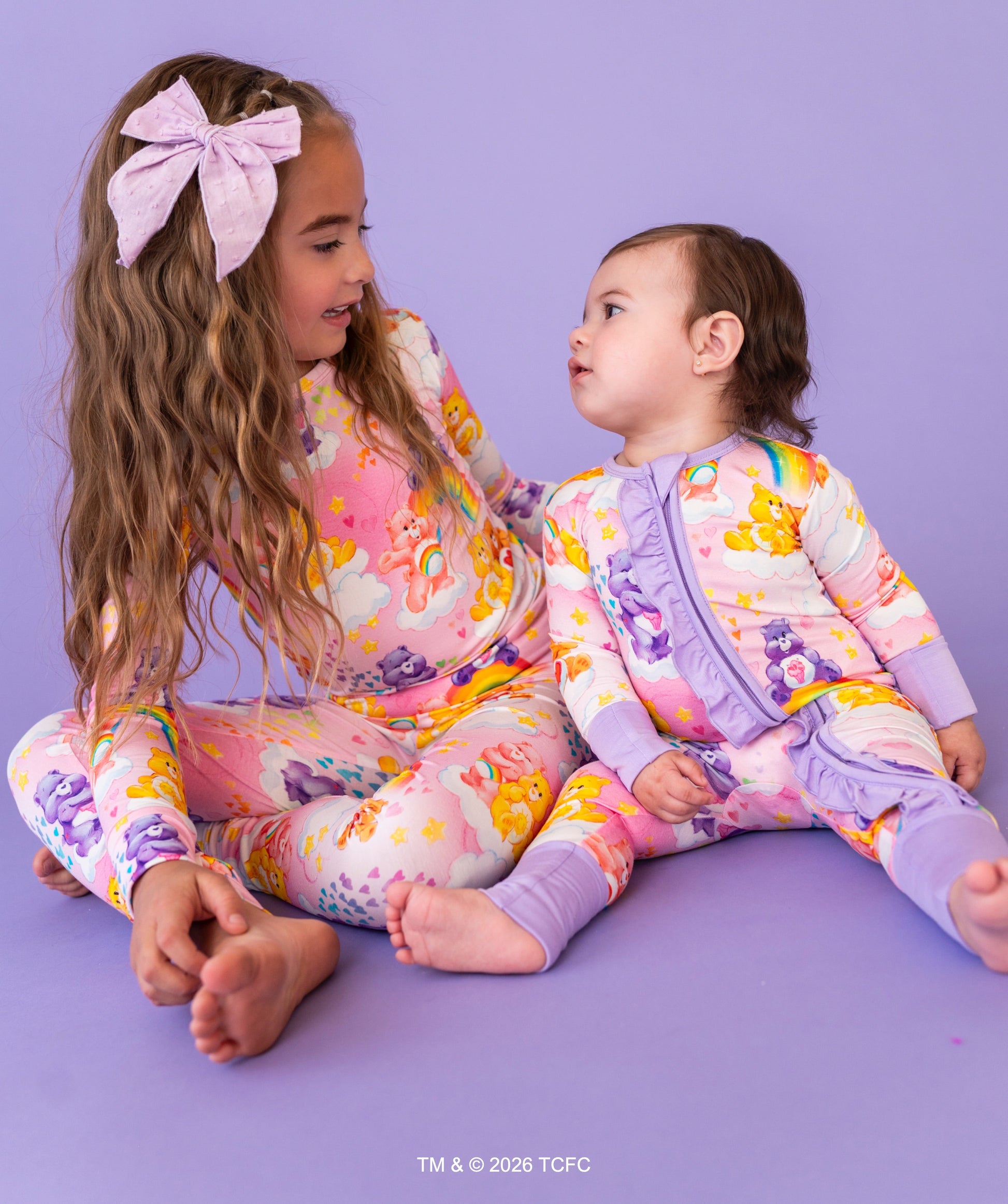 Two children wearing colorful pajamas sitting on a purple floor.