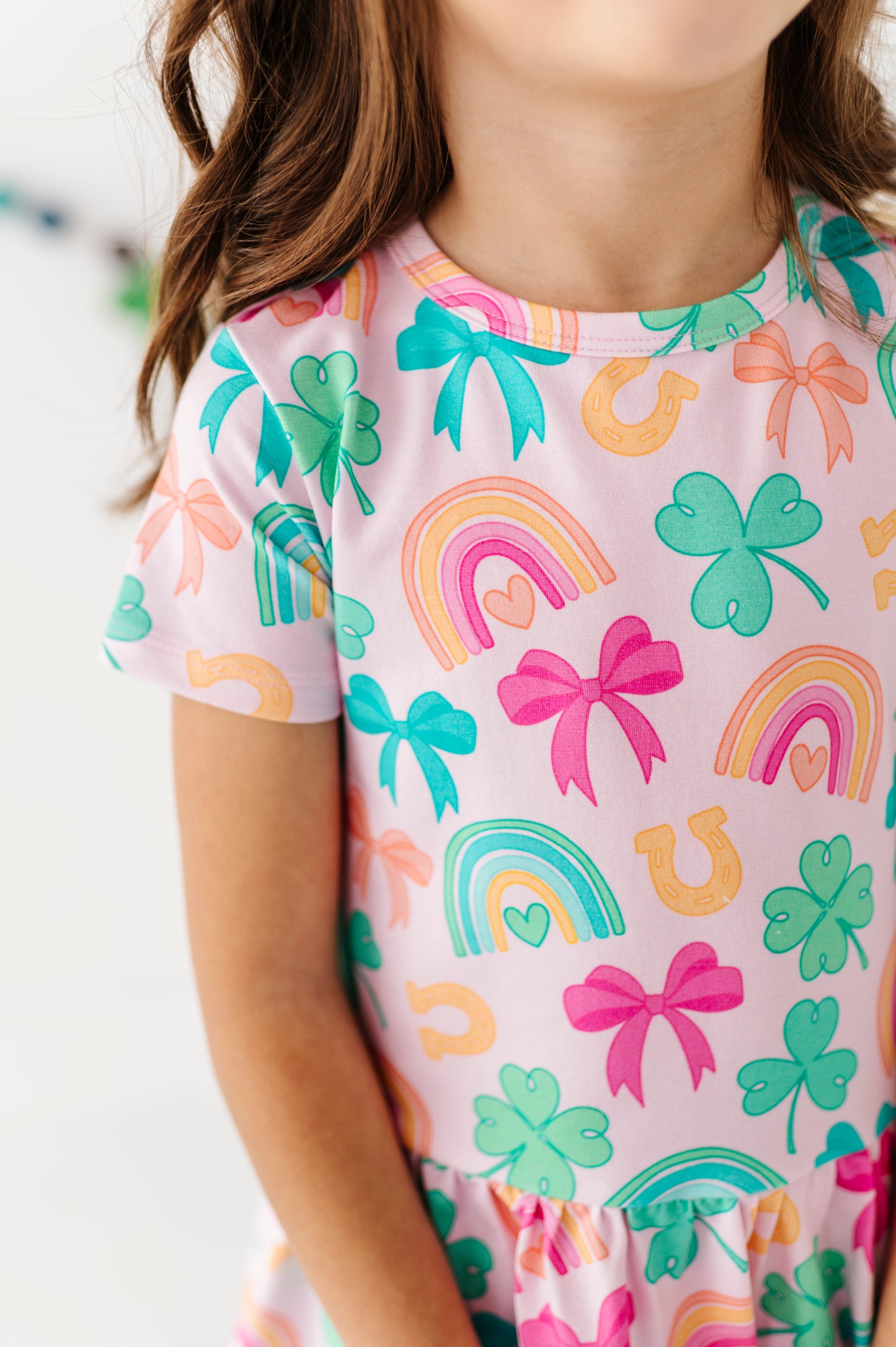 Detail photo of a child wearing a peplum top with colorful patterns including rainbows, shamrocks, and bows.