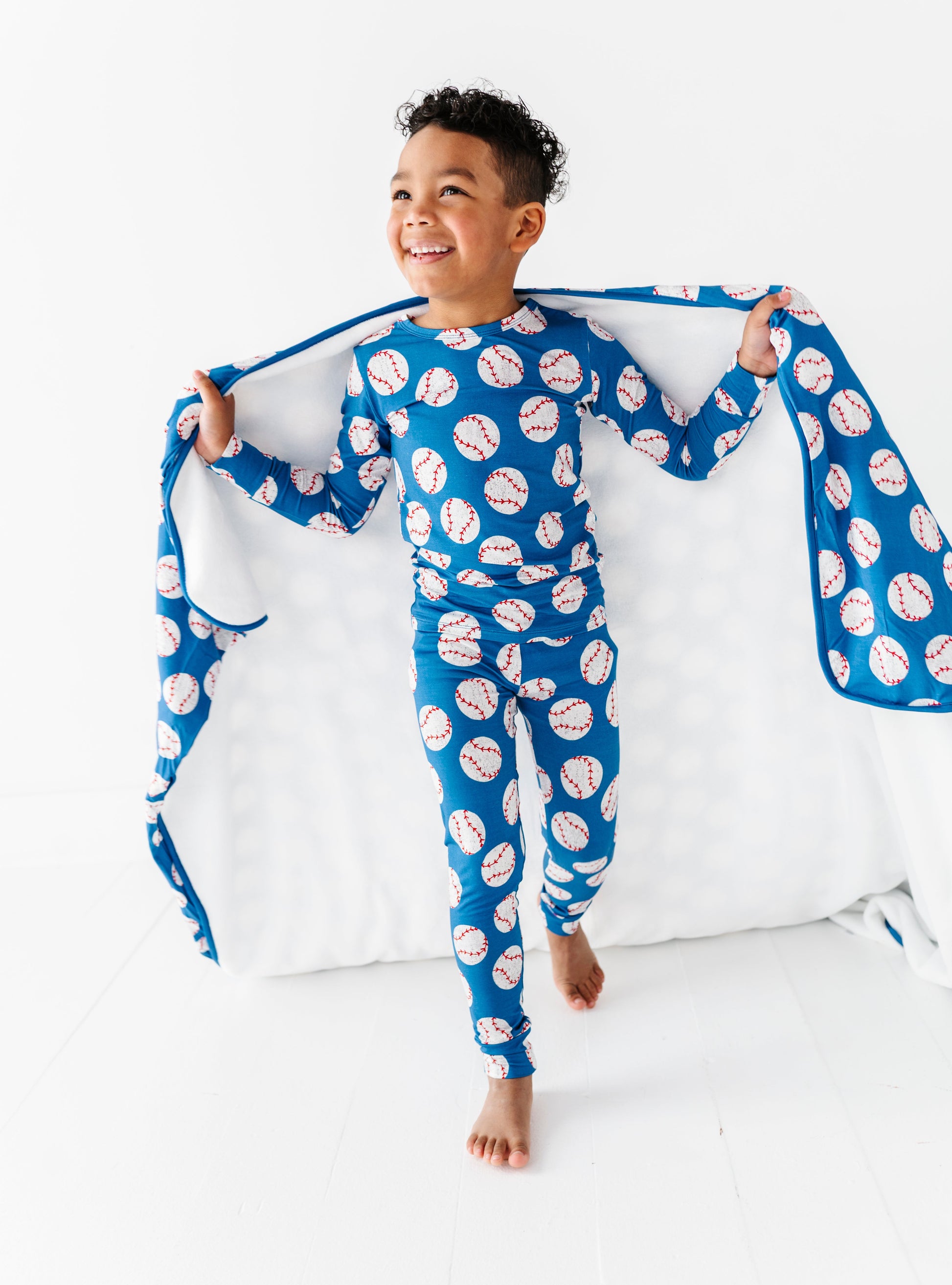 Child wearing a blue pajama set with white and red baseball, holding a matching bamboo blanket.