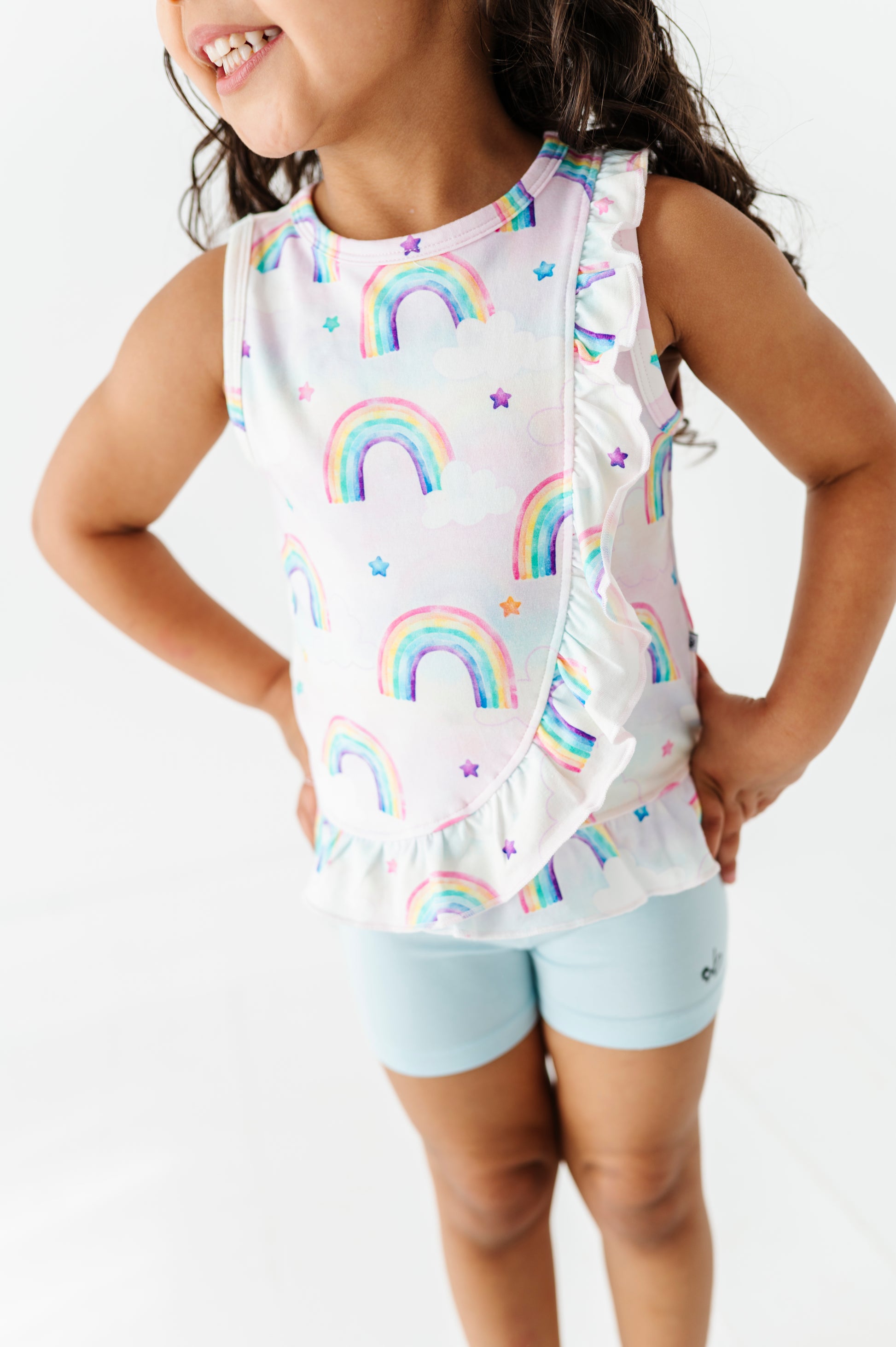Child wearing a sleeveless bamboo cotton peplum top with watercolor rainbow pattern and light blue bamboo biker shorts on a white background