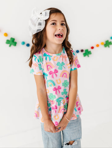 Young girl wearing a colorful lucky charm bamboo/cotton peplum shirt on a white background.