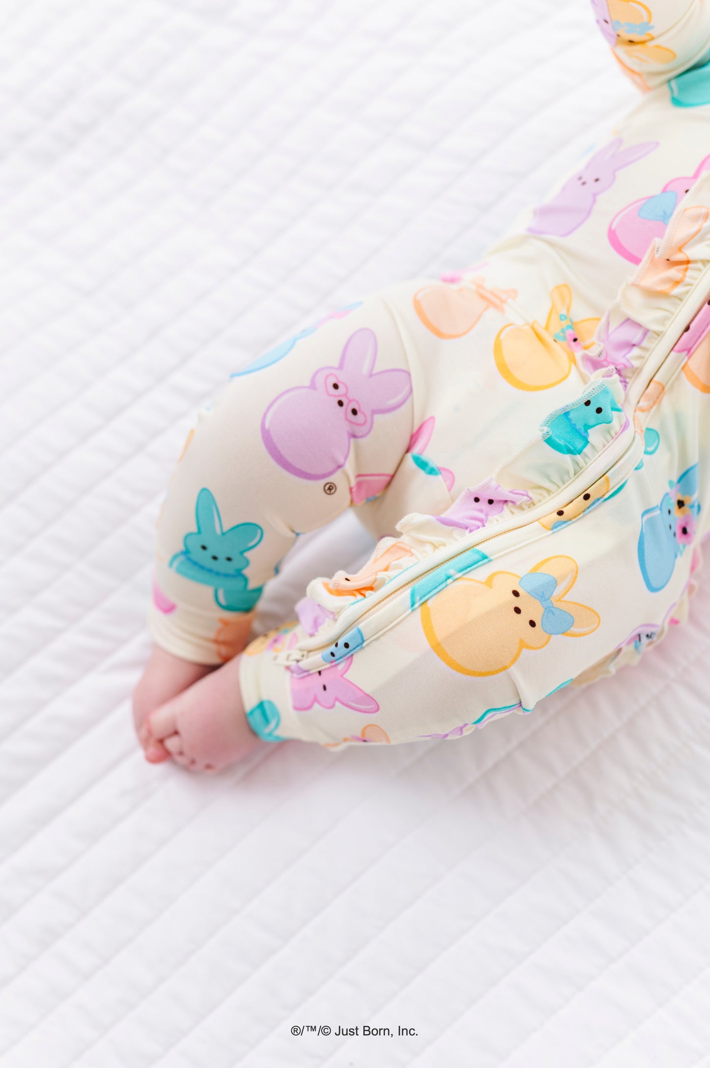 Baby in colorful PEEPS® bunny-themed romper on a white sheet