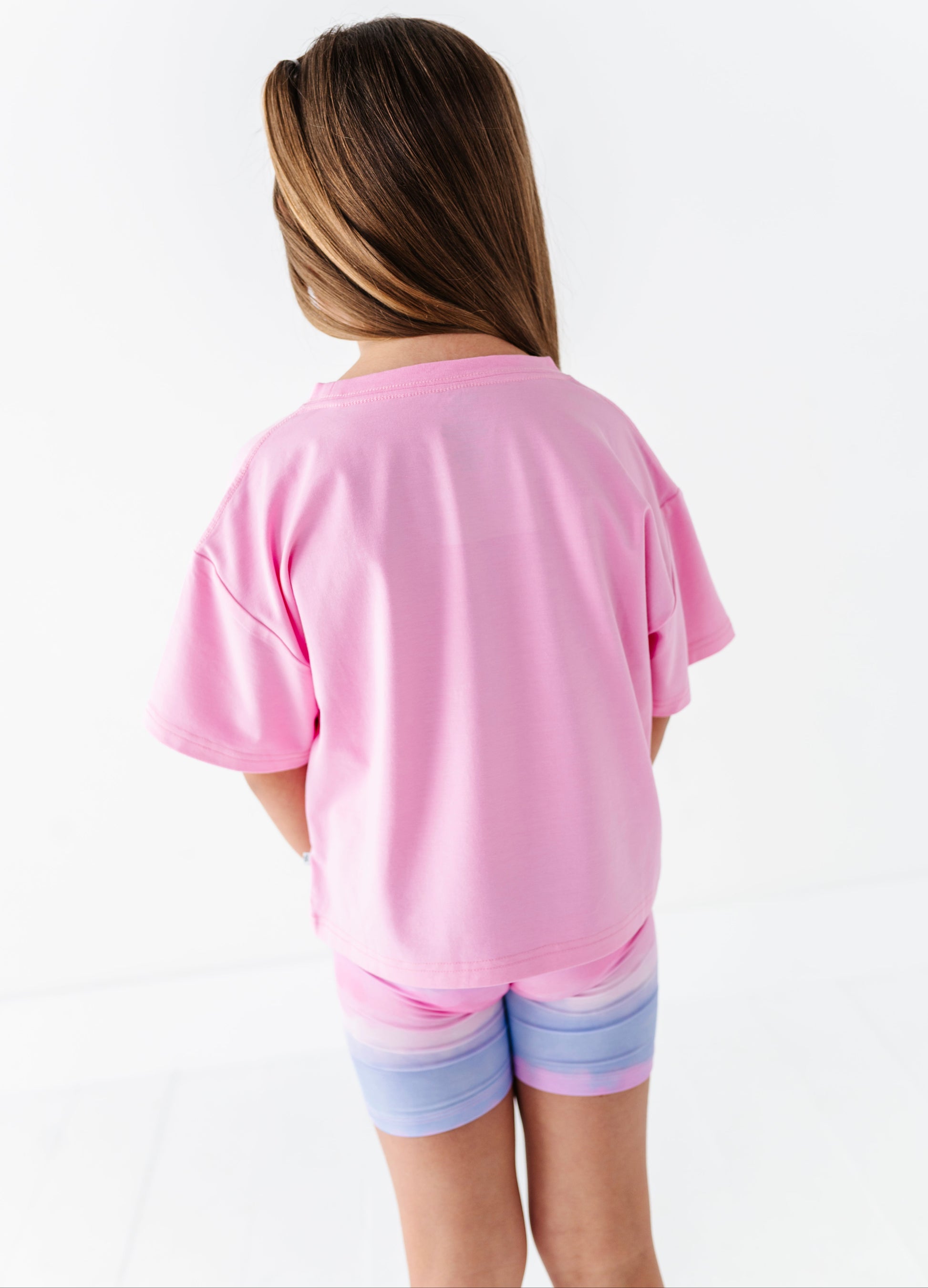 Little girl wearing a pink shirt and colorful shorts on a white background
