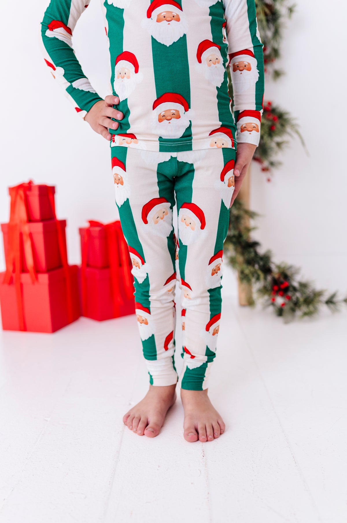 A close-up photo of a boy wearing green-and-beige striped bamboo pajamas with Santa faces all over them. The super soft bamboo pajamas are ribbed and made to fit snugly for safety standards