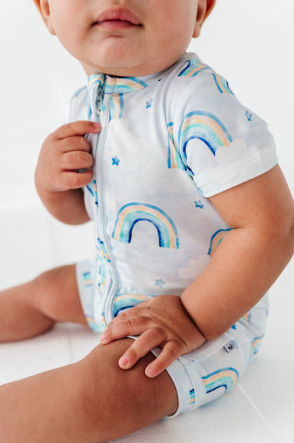Baby wearing a bamboo shortie zip romper with watercolor rainbow patterns on a white background